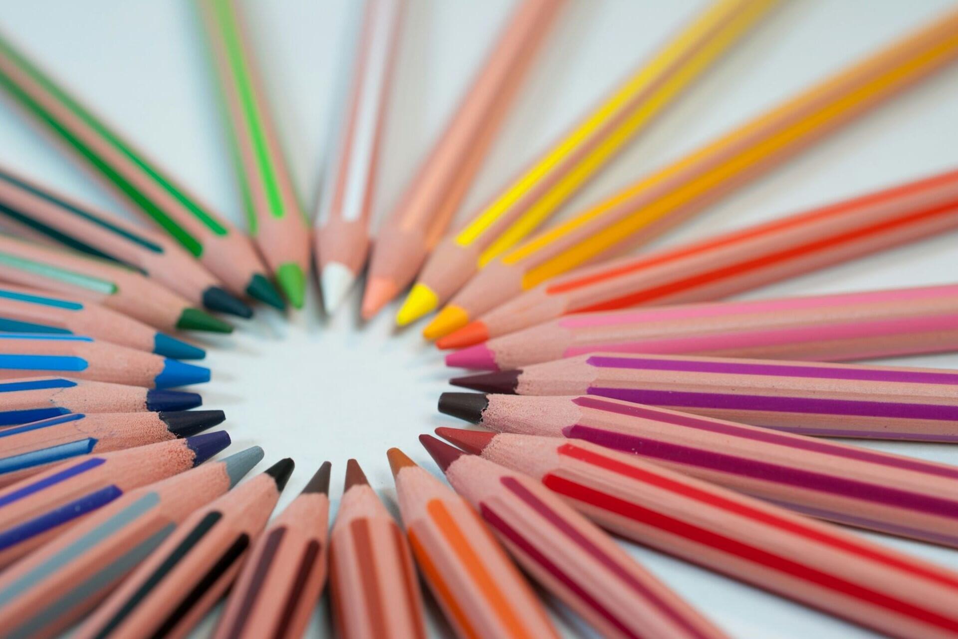 Close-up of coloured pencils arranged in a circular pattern on a white background.