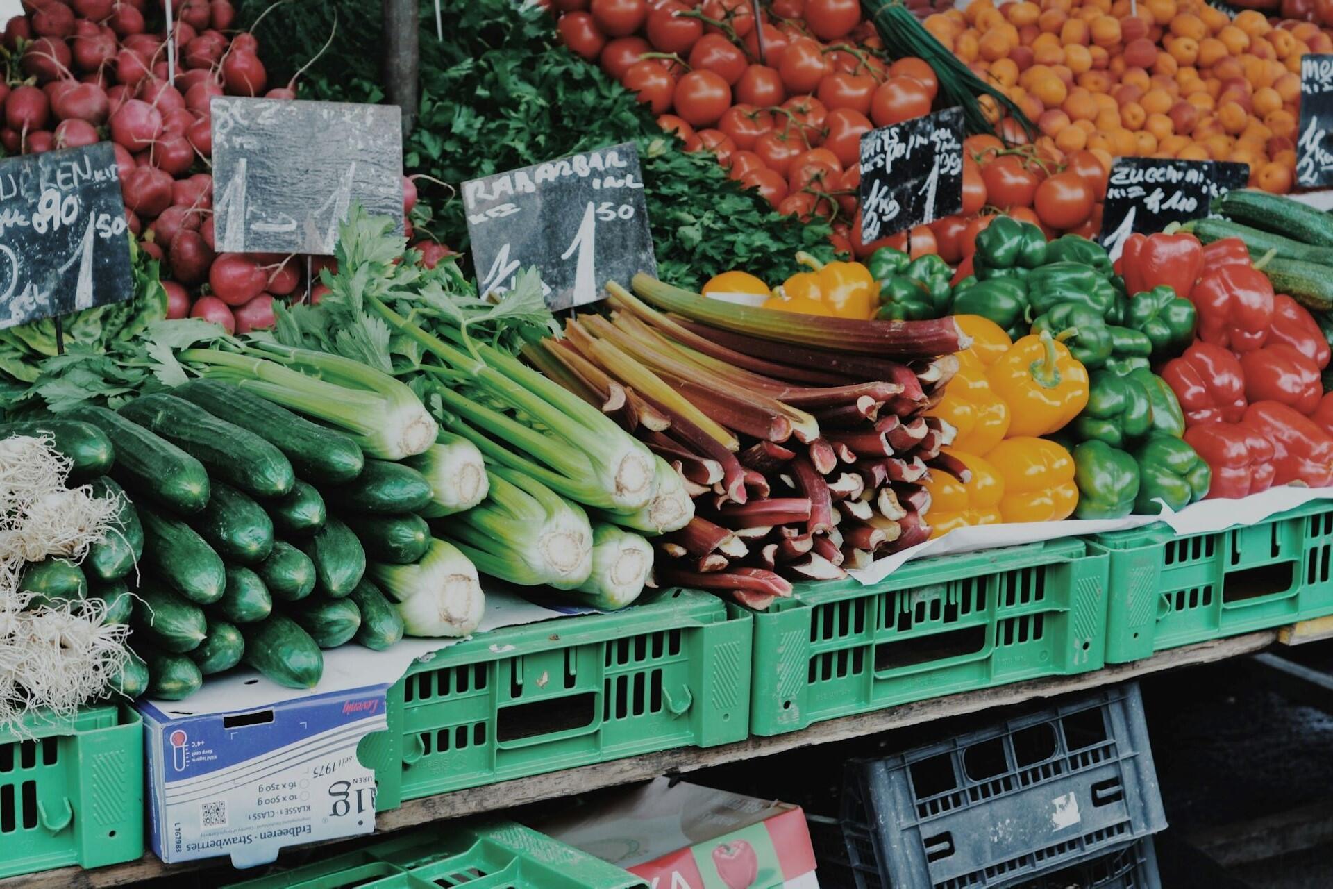 Colorful vegetables arranged on crates at an outdoor market stall with price signs.