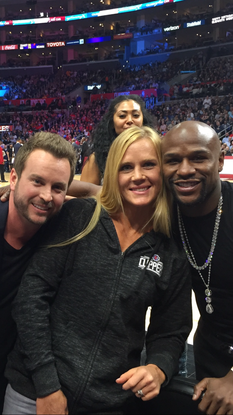 Holly Holm and Floyd Mayweather smiling together with another man at a Clippers basketball game.