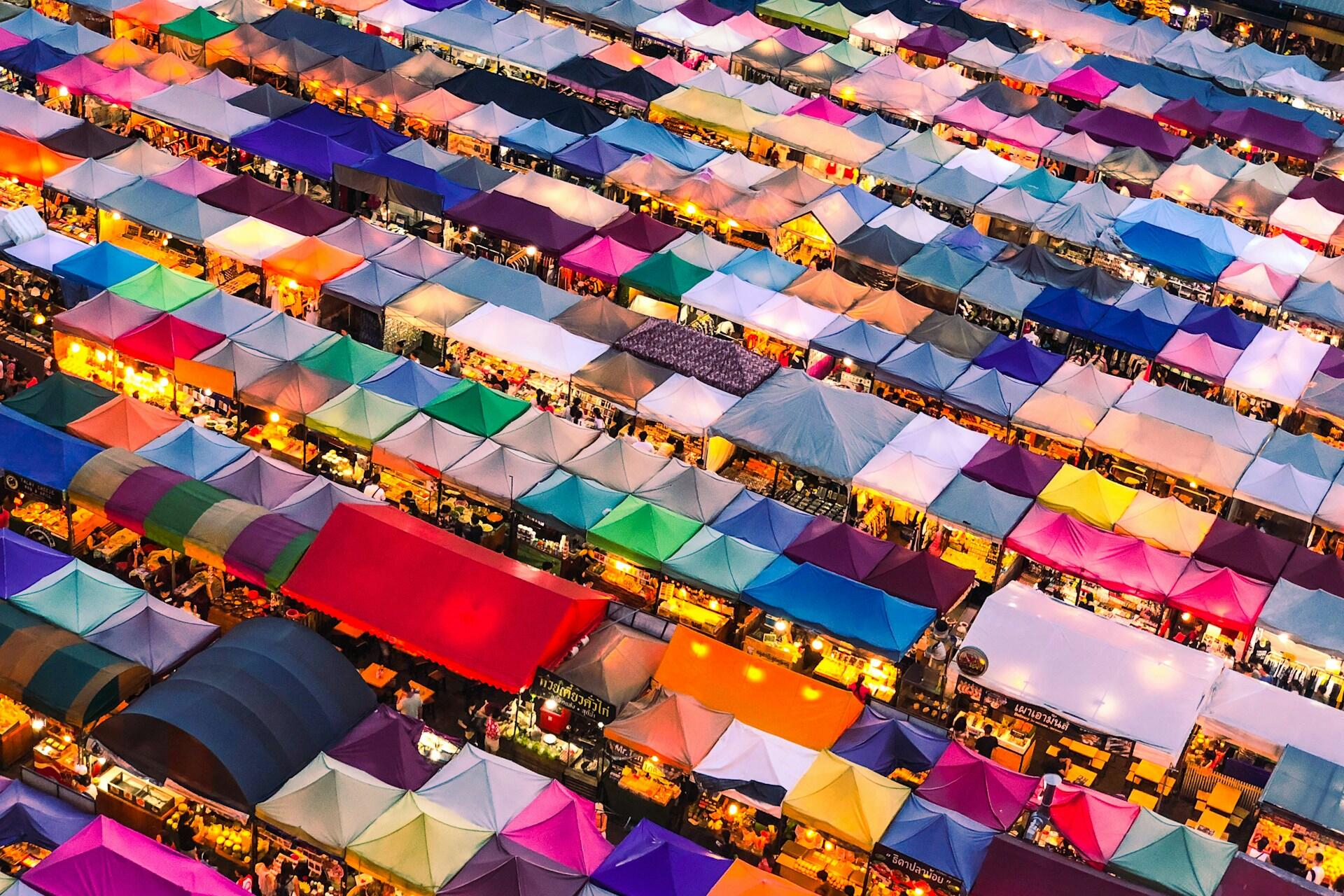 Aerial view of a busy outdoor market with rows of colourful tents and illuminated stalls at night.