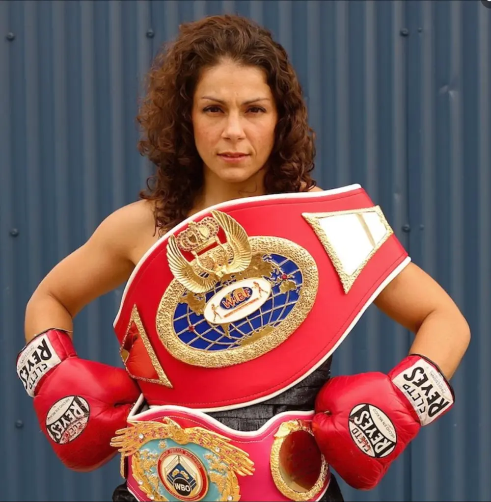 Melissa McMorrow wearing red boxing gloves and showing off two belts.