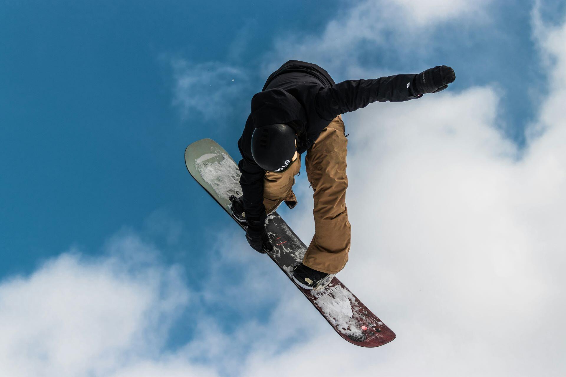 Snowboarder performing a jump in mid-air against a blue sky.