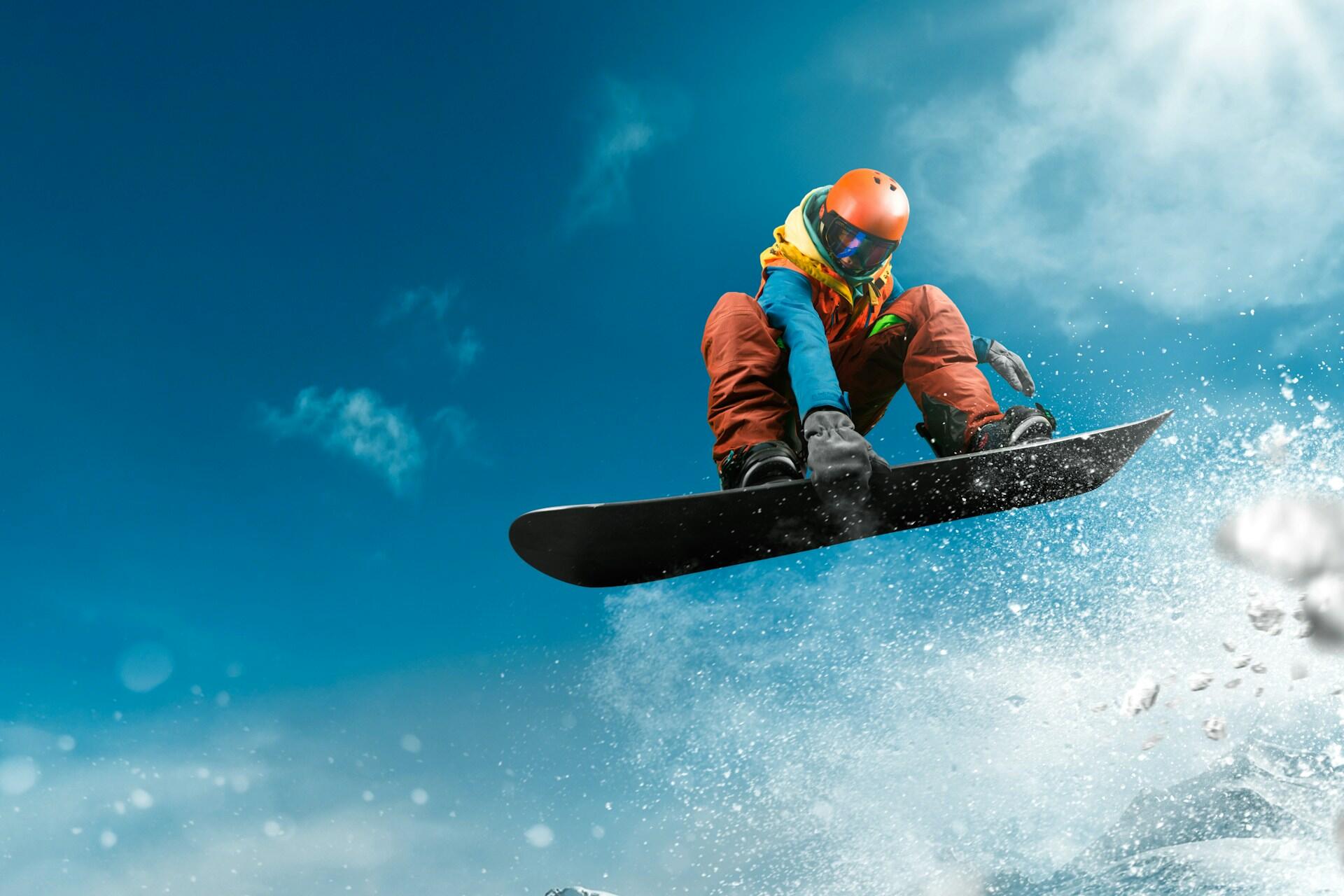 A man in an orange snowsuit snowboarding in the air.