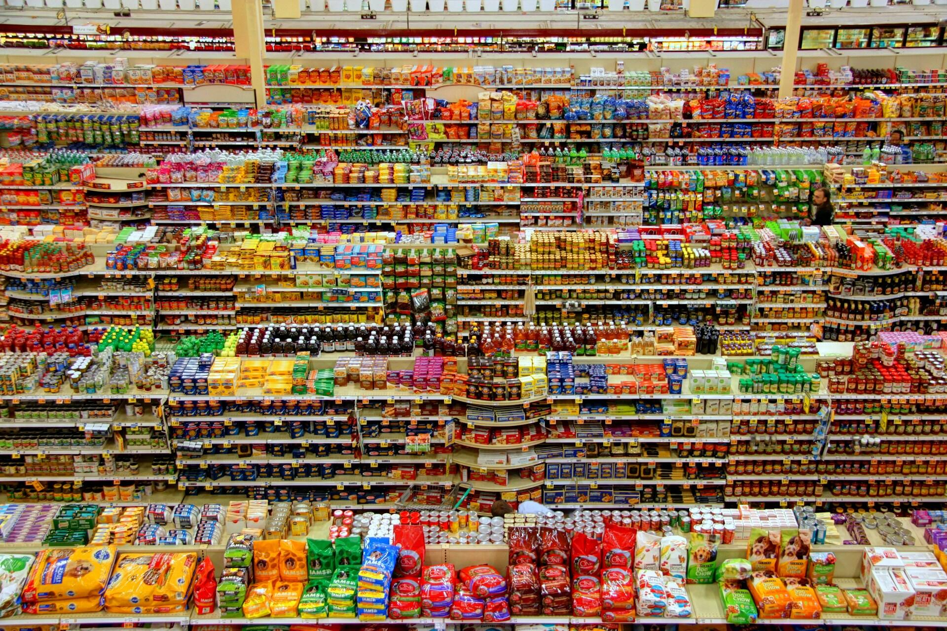 Wide view of a supermarket aisle filled with packaged food products on shelves.