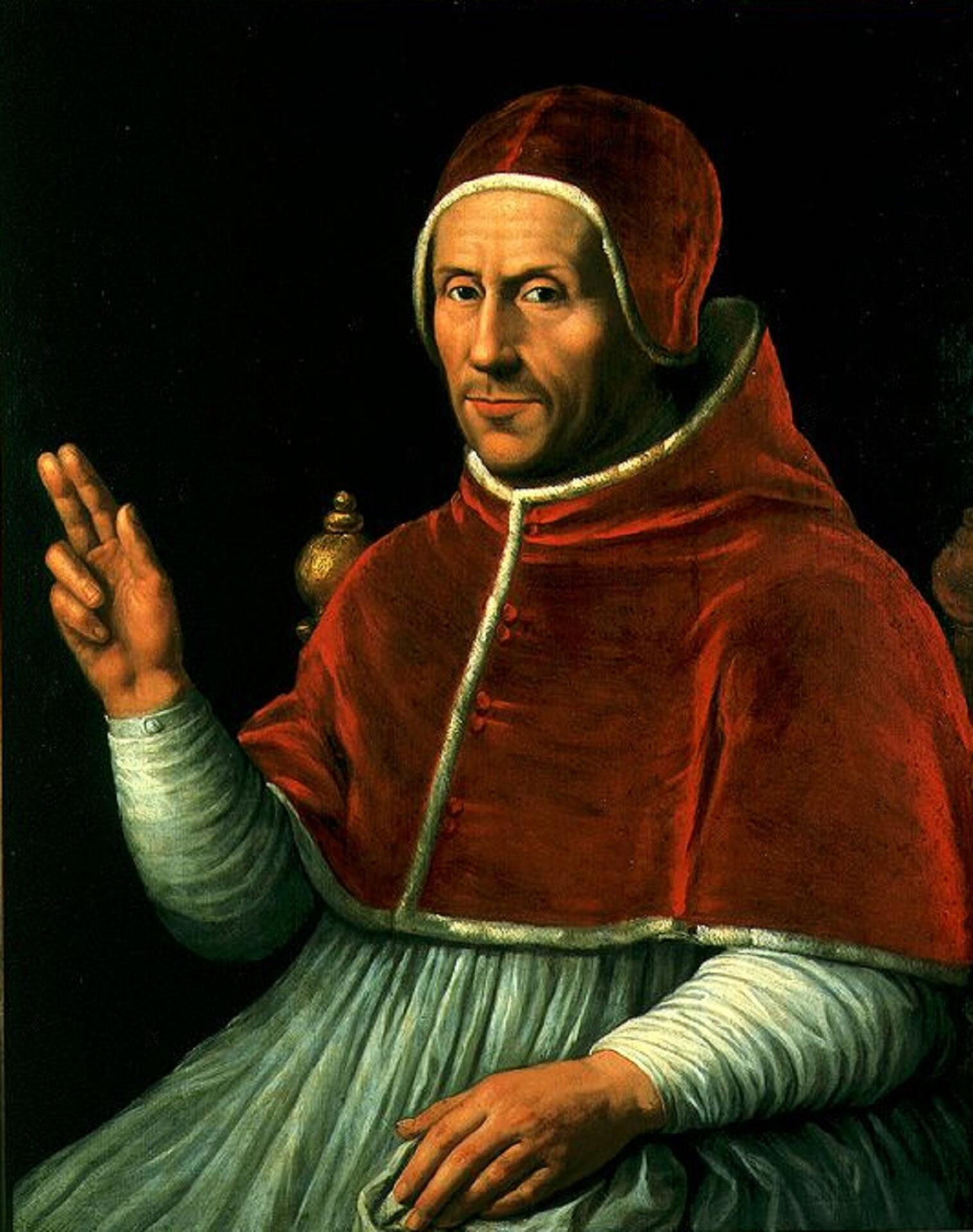 A man in a red jacket and papal robe makes a hand sign. 