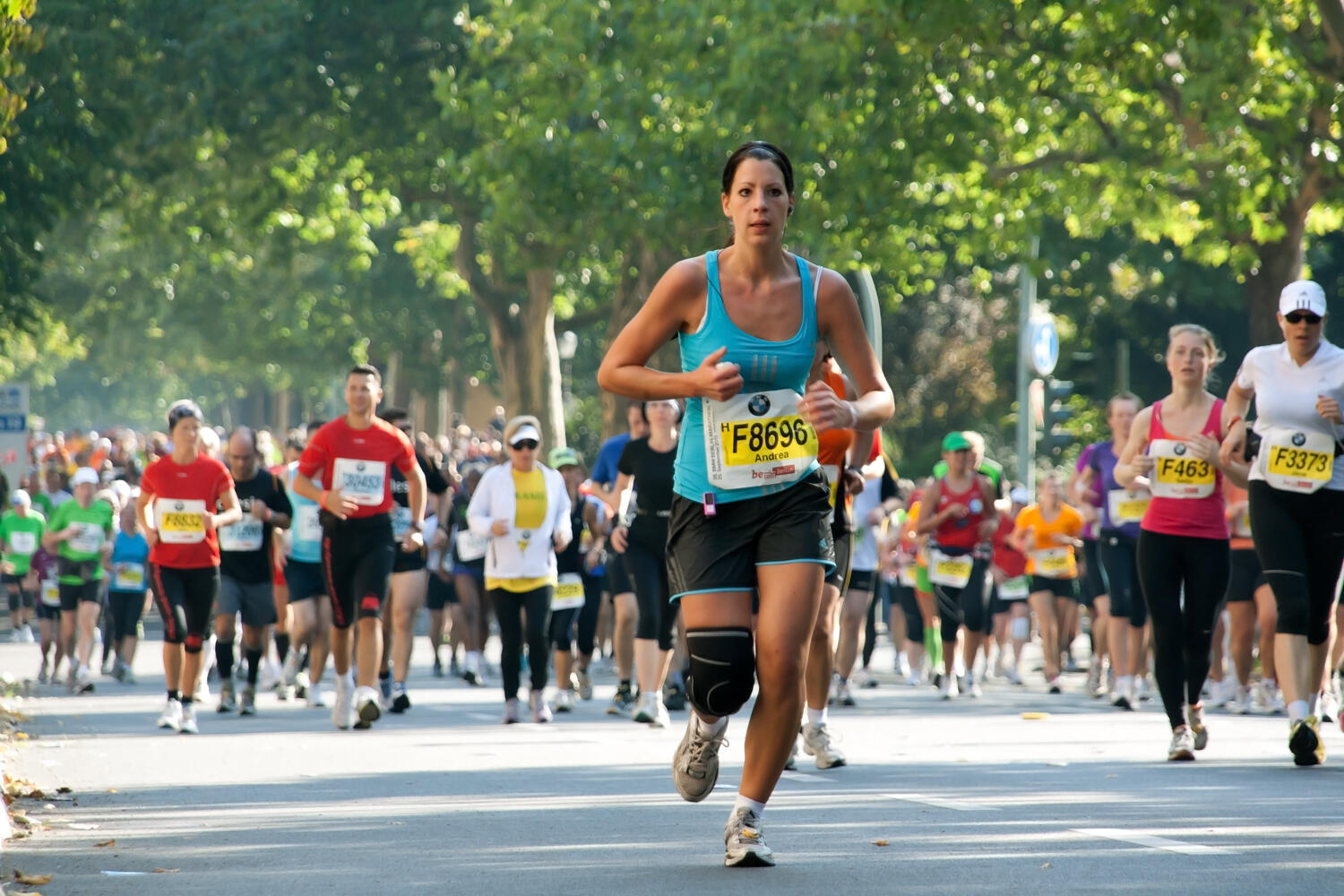 Runners passing under green trees in the Berlin Marathon