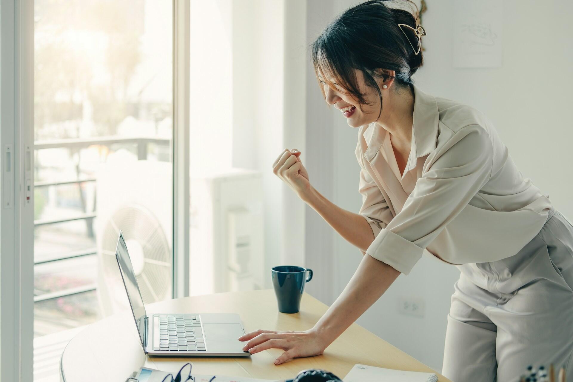 person looking at a computer, standing up and pumping their fist, smiling