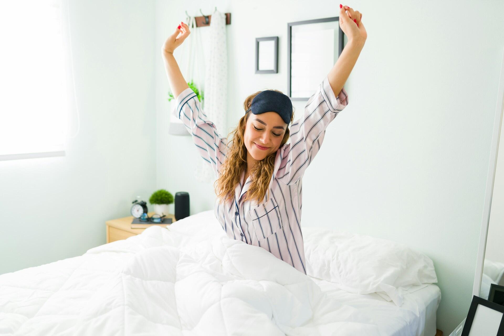 person waking up well rested, a sleep mask on their head, stretching and smiling