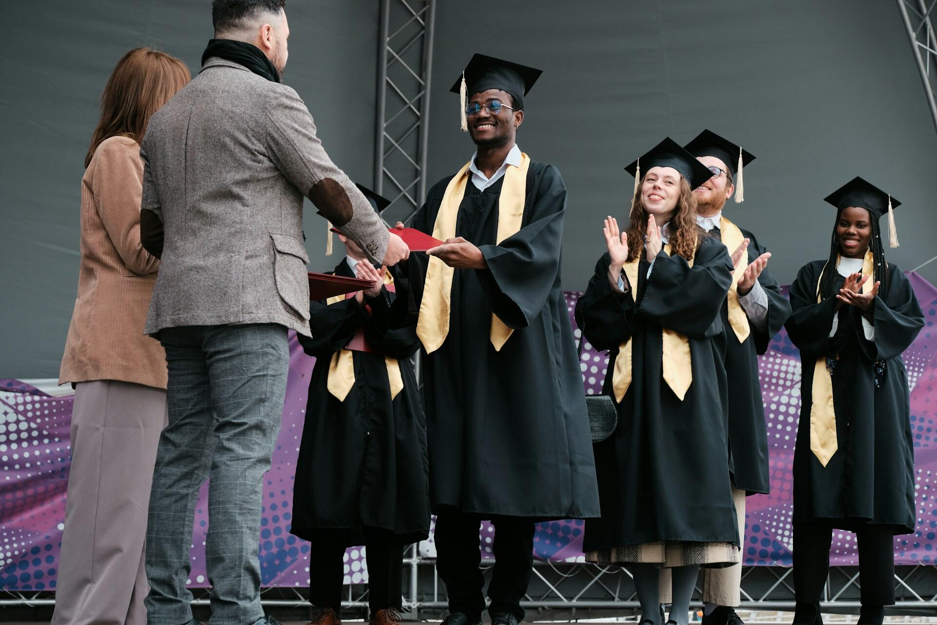 college graduates being handed their degrees on stage