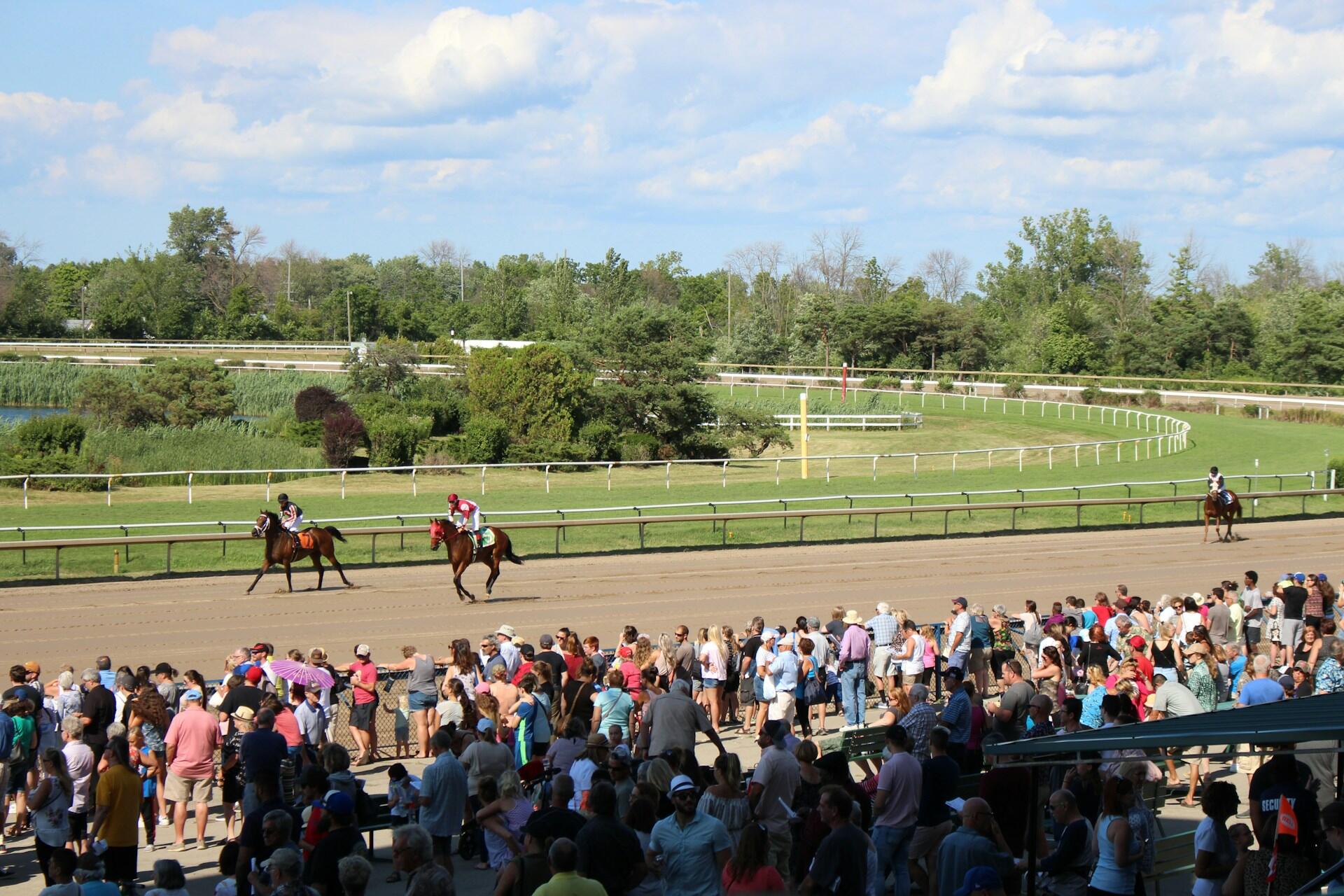 Spectators watching three horses and their jockeys race in the Kentucky Derby.