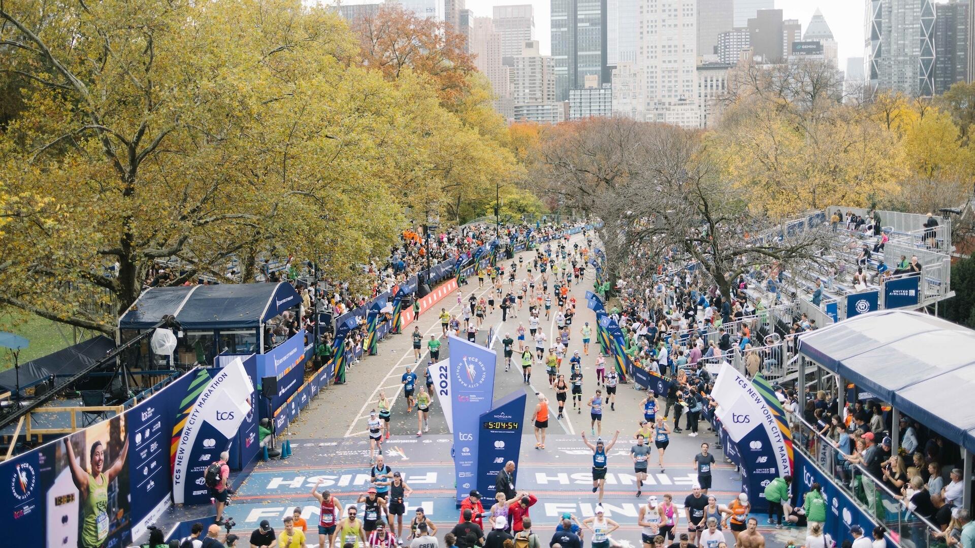 runners crossing the New York City Marathon finish line in Central Park with the city skyline in the background