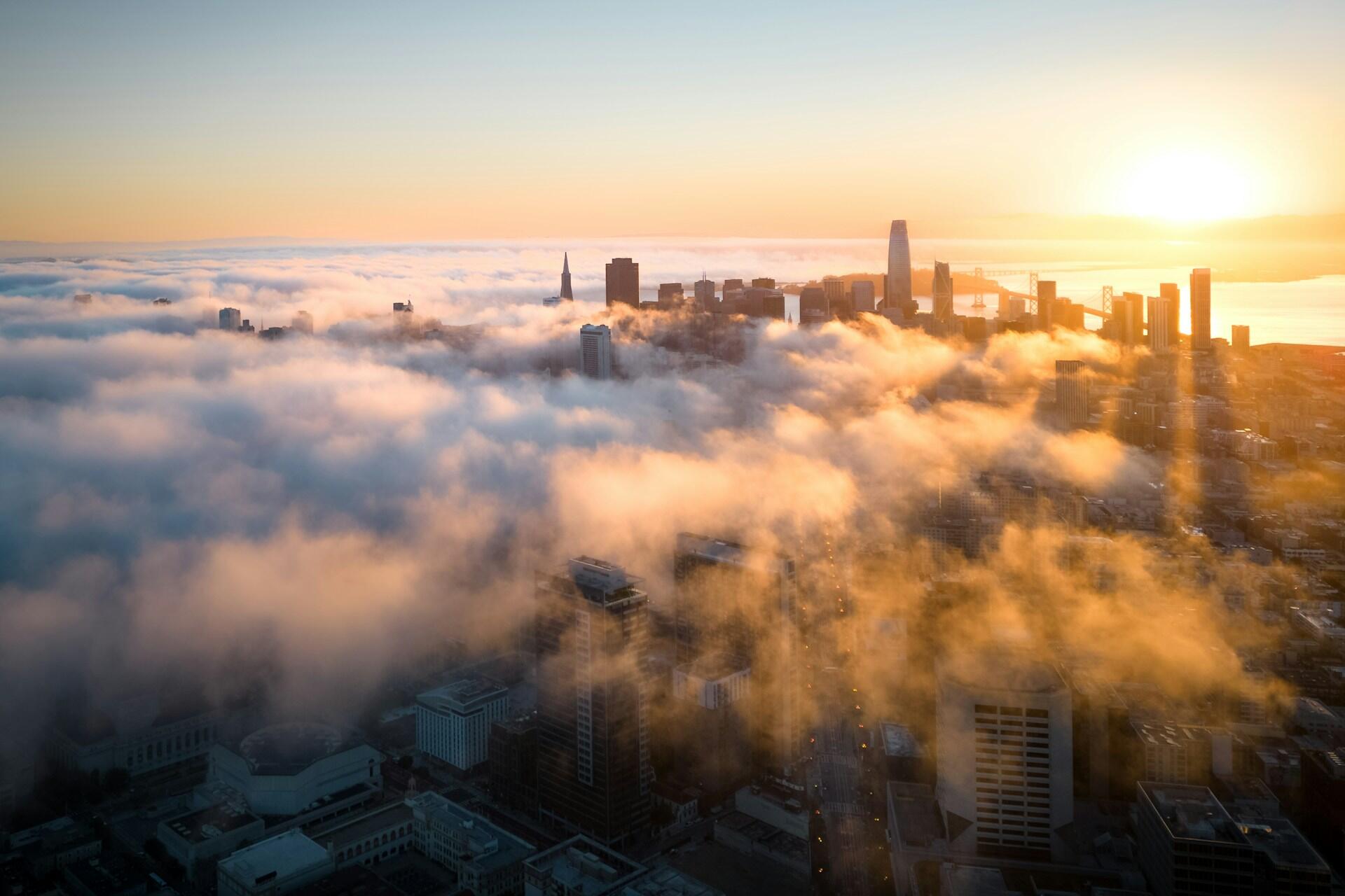 San Francisco skyline emerging through fog at sunrise with city buildings and bay bridge visible