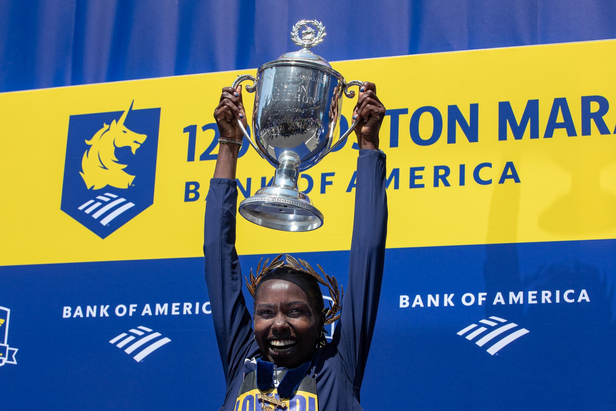 Sharon Lokedi holding up the trophy in front of the Boston Marathon finish sign