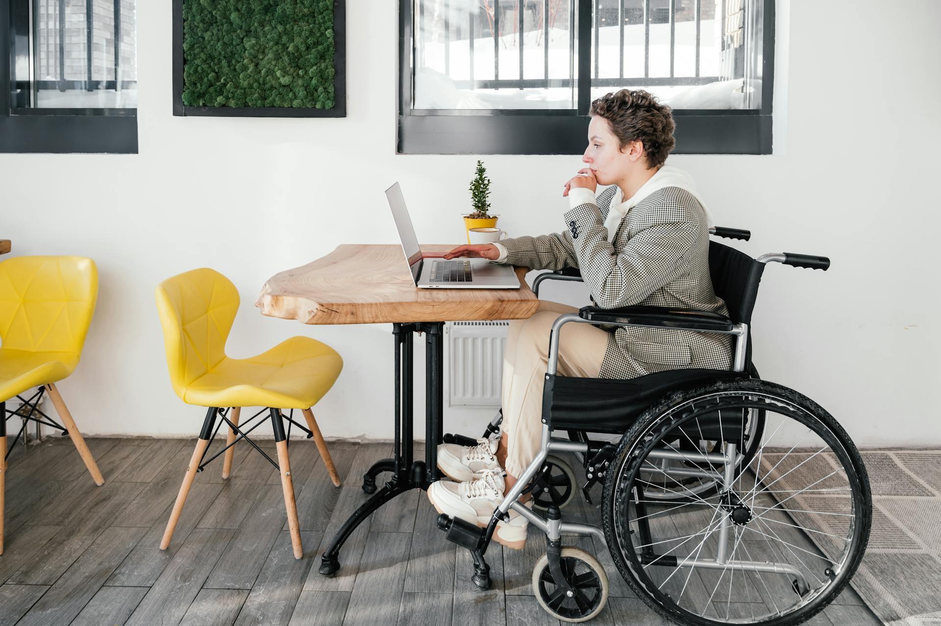 person in a wheelchair using a laptop computer at a table