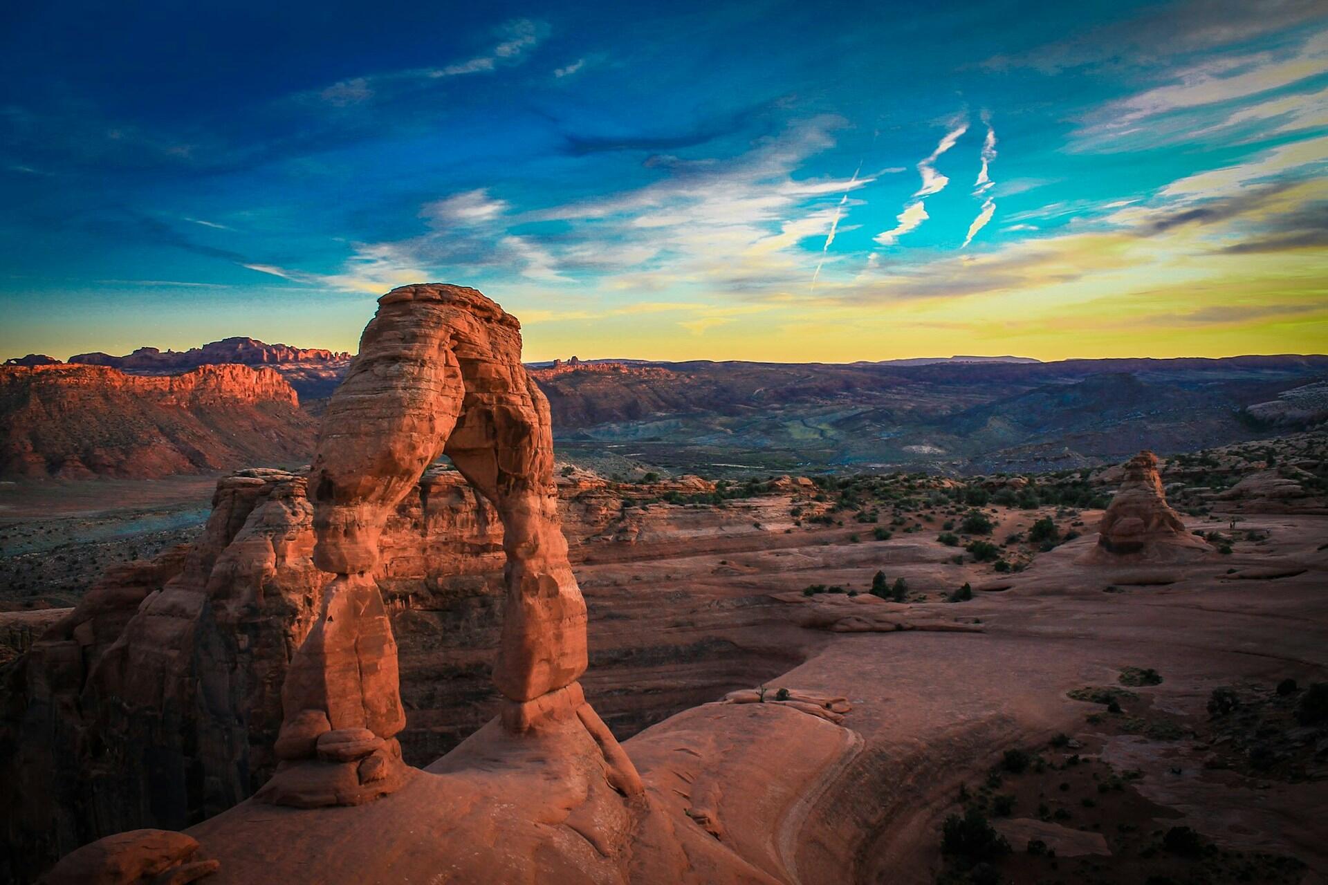 sunset over a red-rock canyon with an arch made of rocks in the foreground