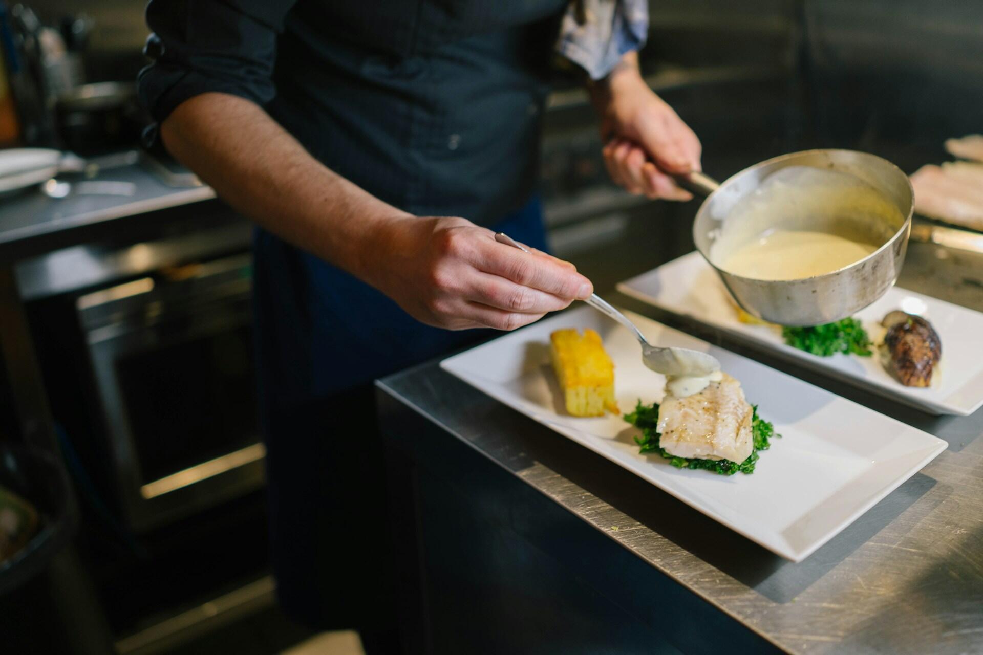 A chef dishing out a sauce on a plate of fish.