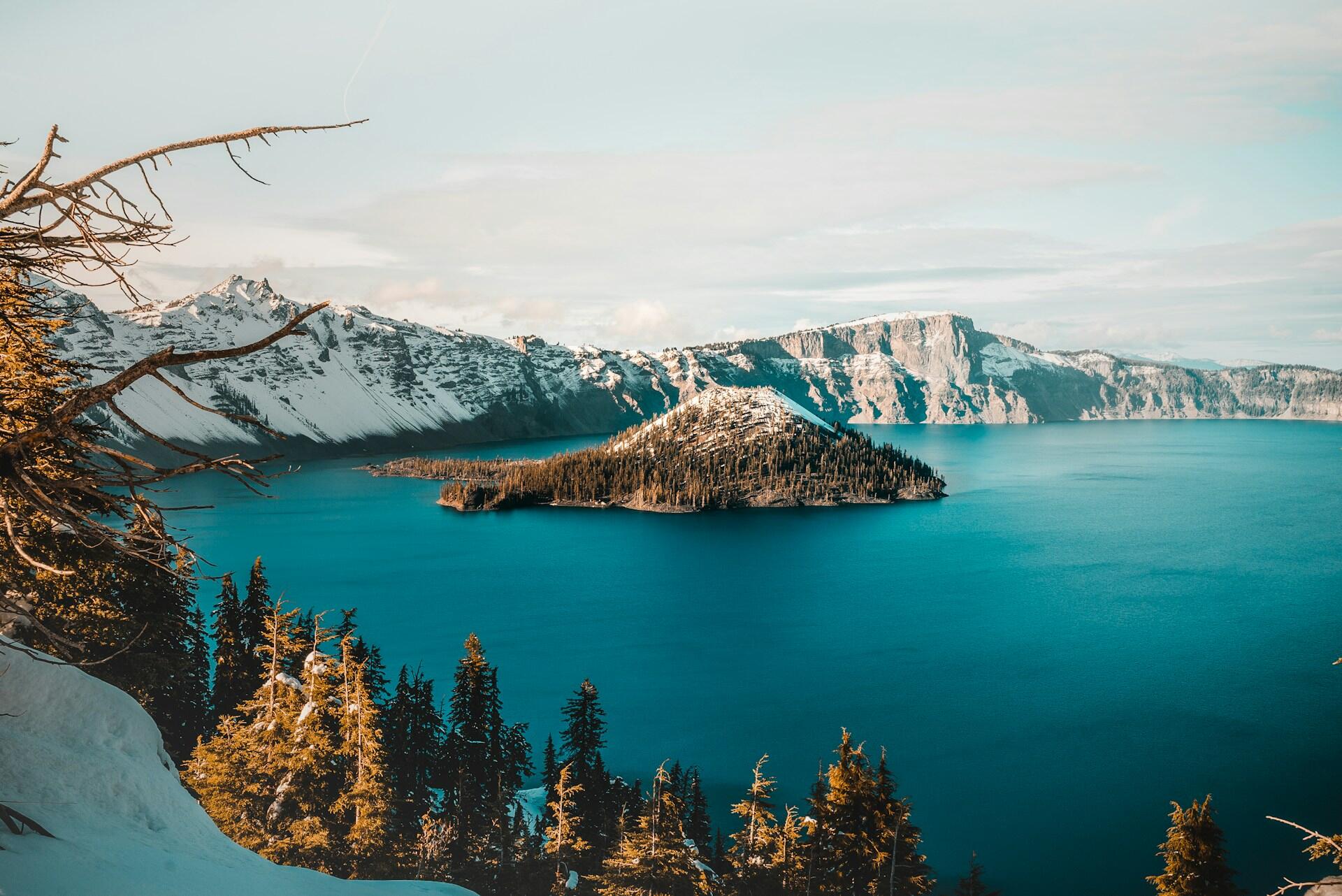 bright blue water of Crater Lake, surrounded by steep , snowy cliffs, with a small island in the center