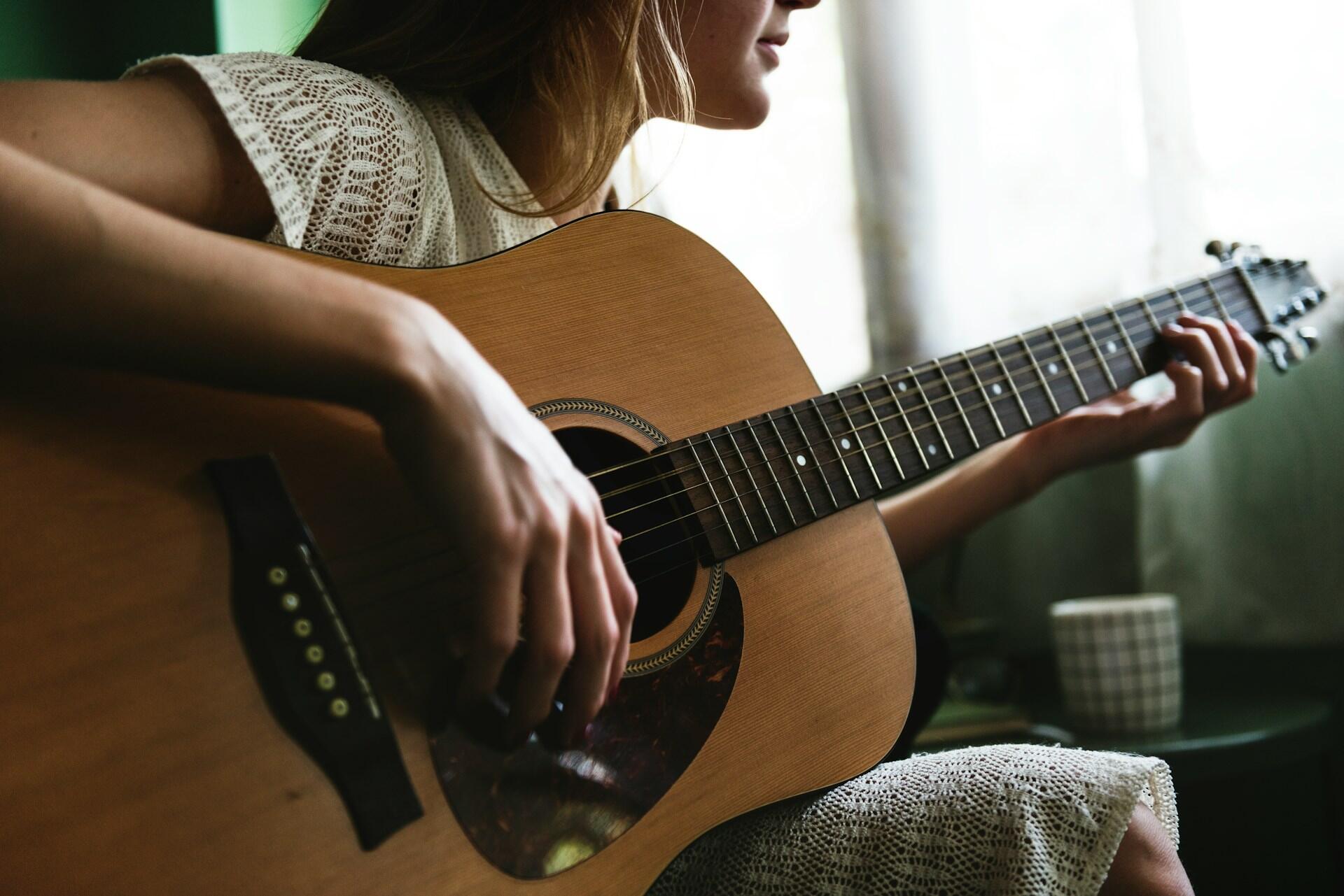 A close up of a girl playing an acoustic guitar with her hand on strumming the strings.