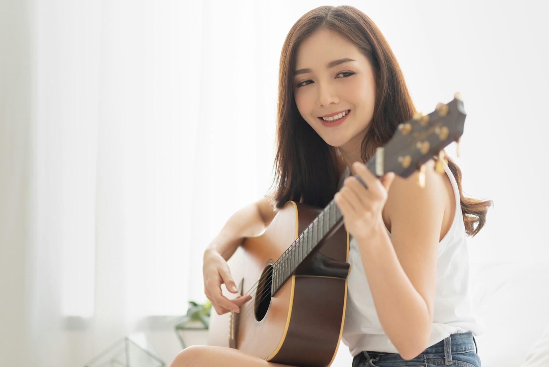 A girl sitting down playing a light brown acoustic guitar.