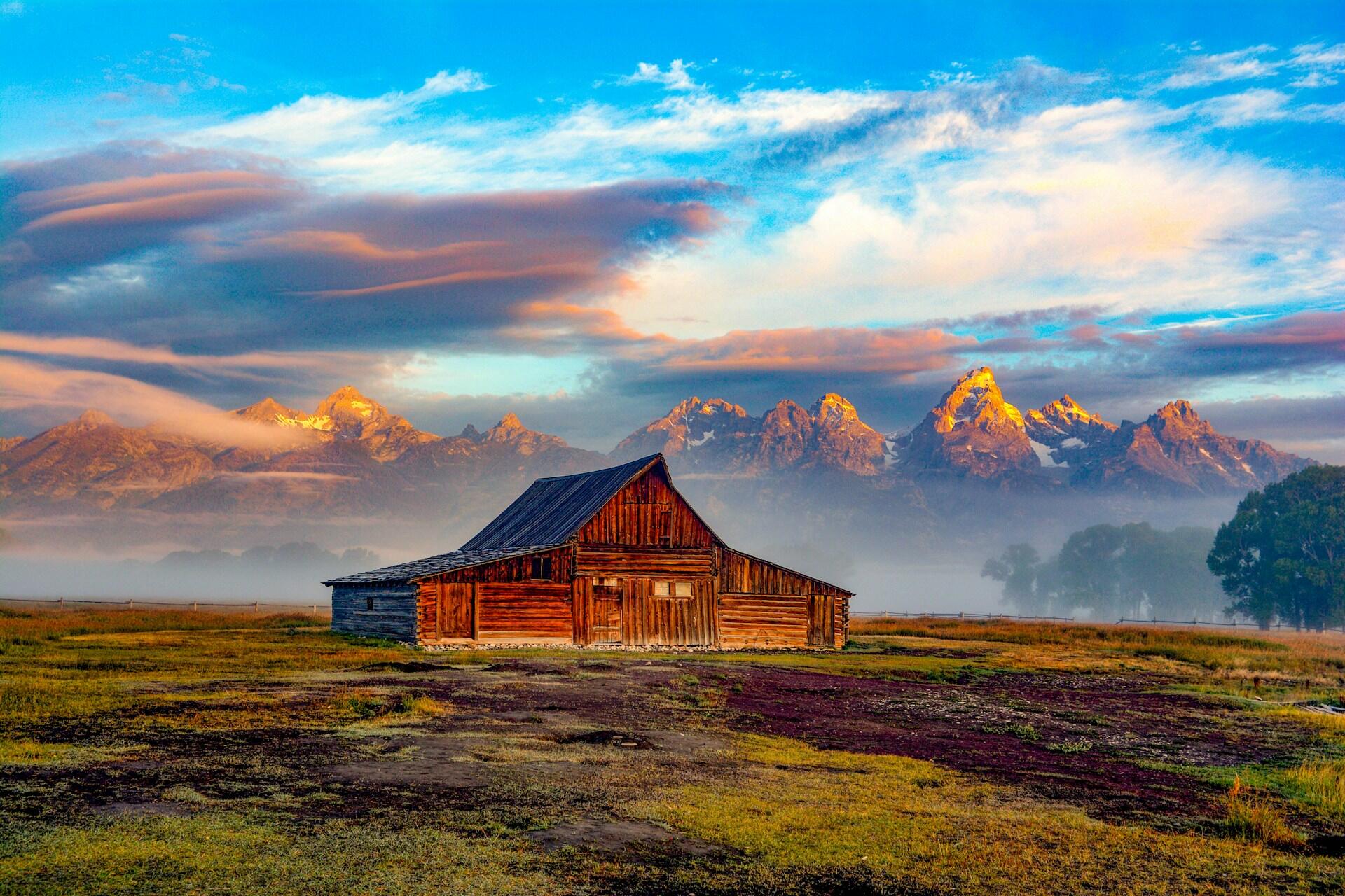 wooden barn on a grassy plain with jagged mountain range in the background