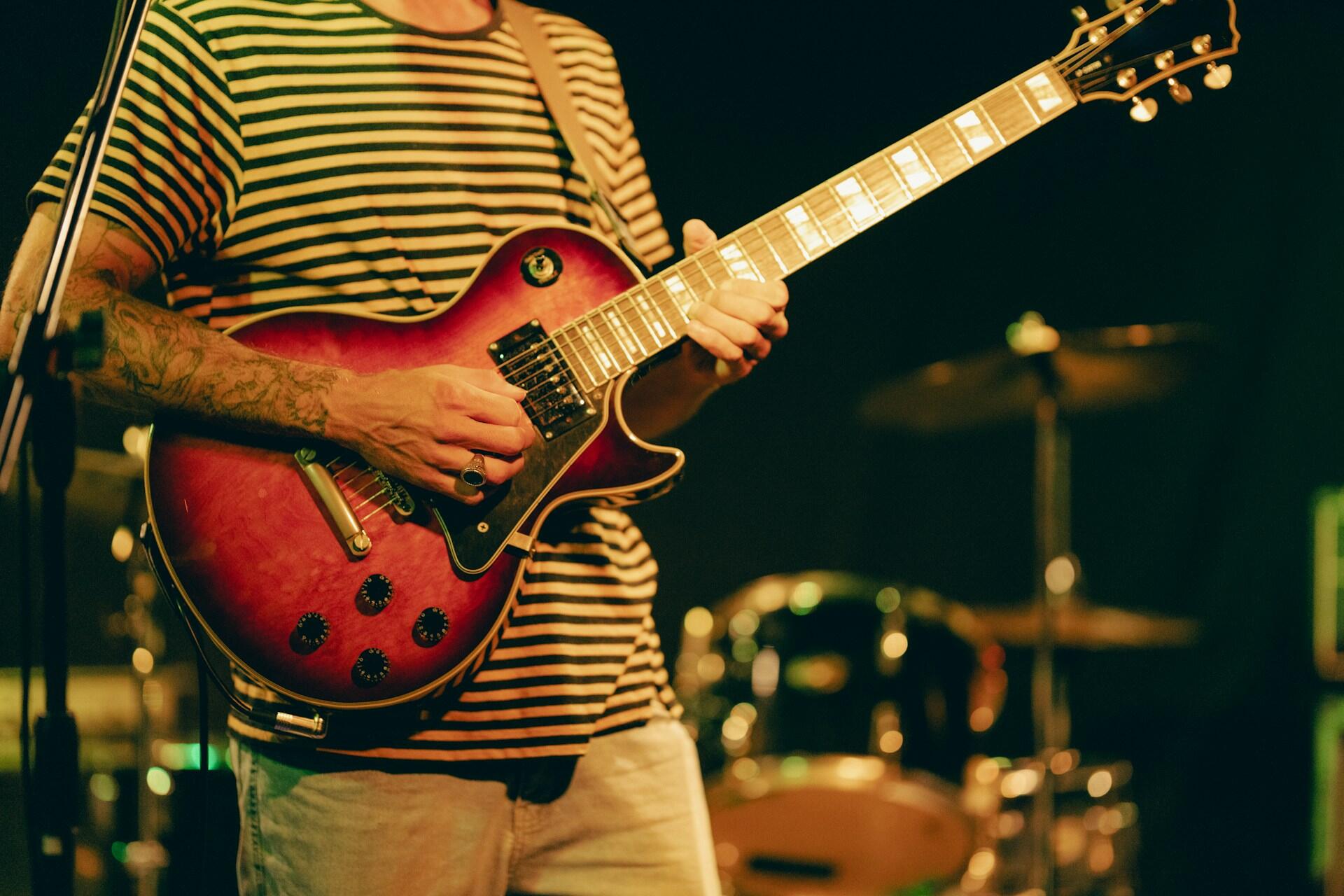 A man in a stripped shirt playing an orange guitar on stage.