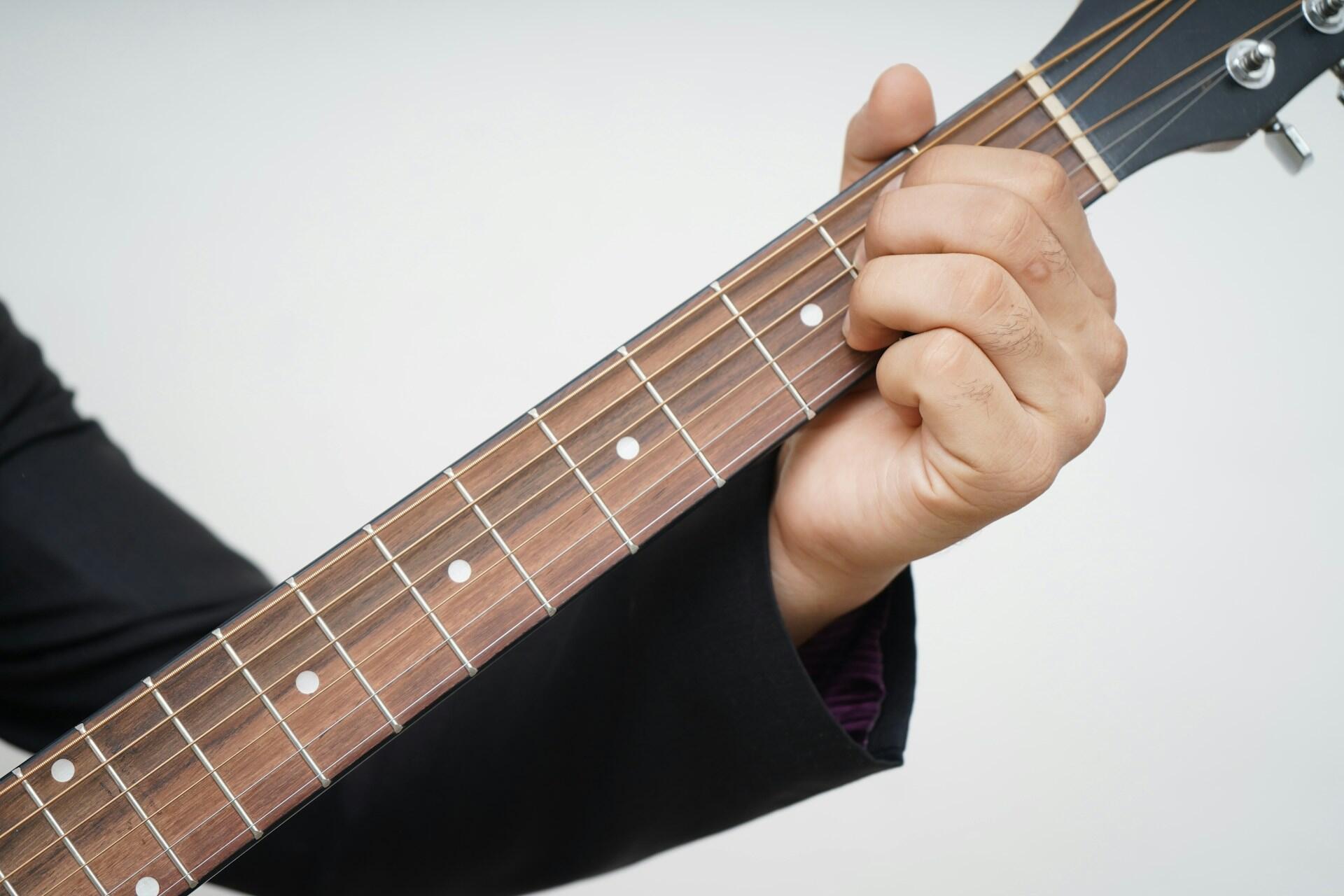 The stem of a guitar and someone holding it.