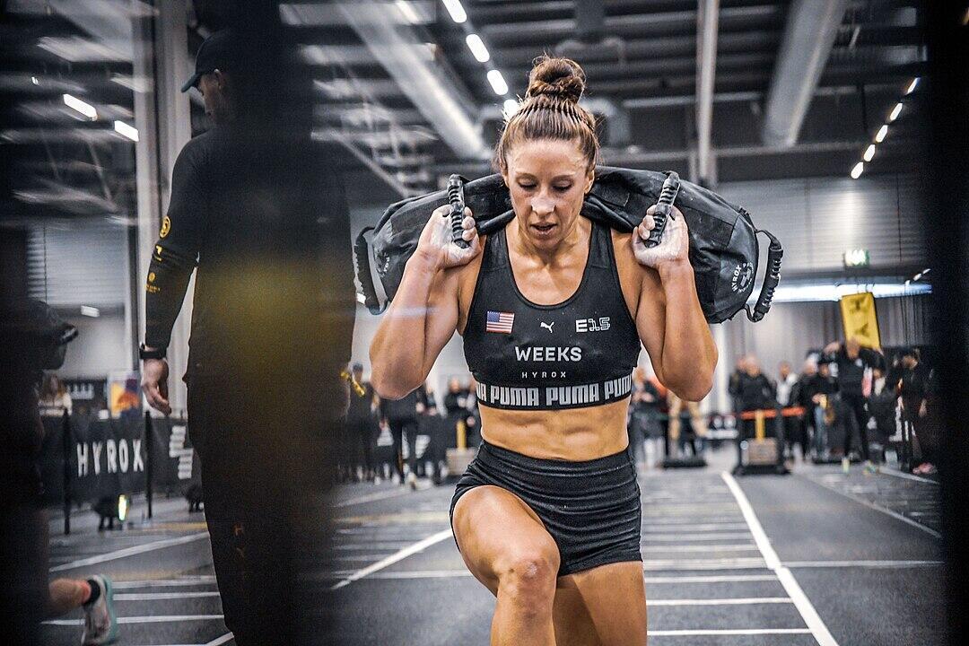 A focused athlete performs a weighted exercise indoors during a competitive event, showcasing strength and determination.