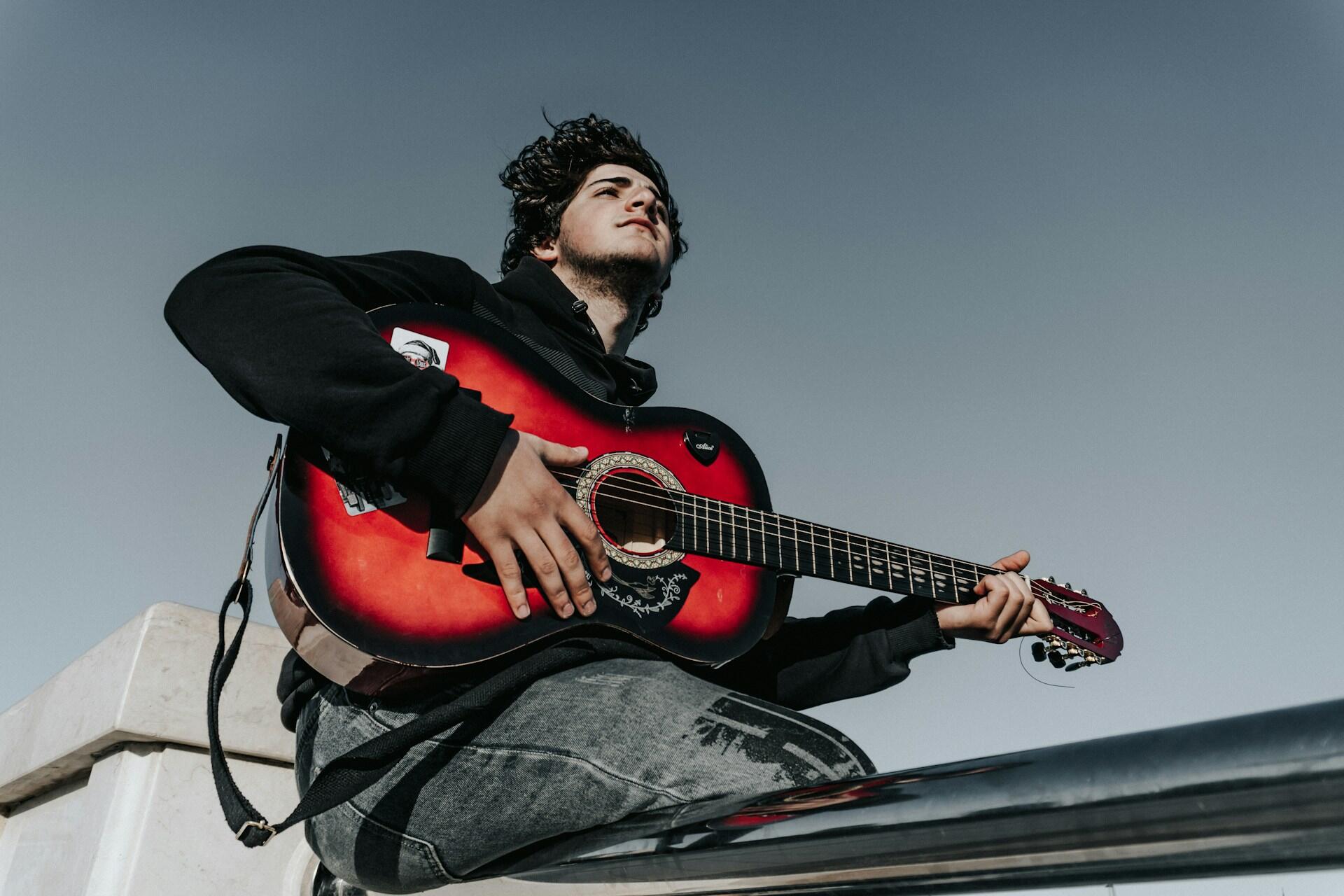 A man looking out into the distance holding a red guitar.