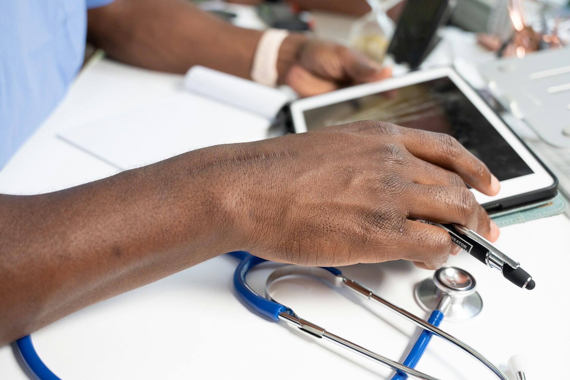 A person working on an iPad with a medical stethoscope on the table.