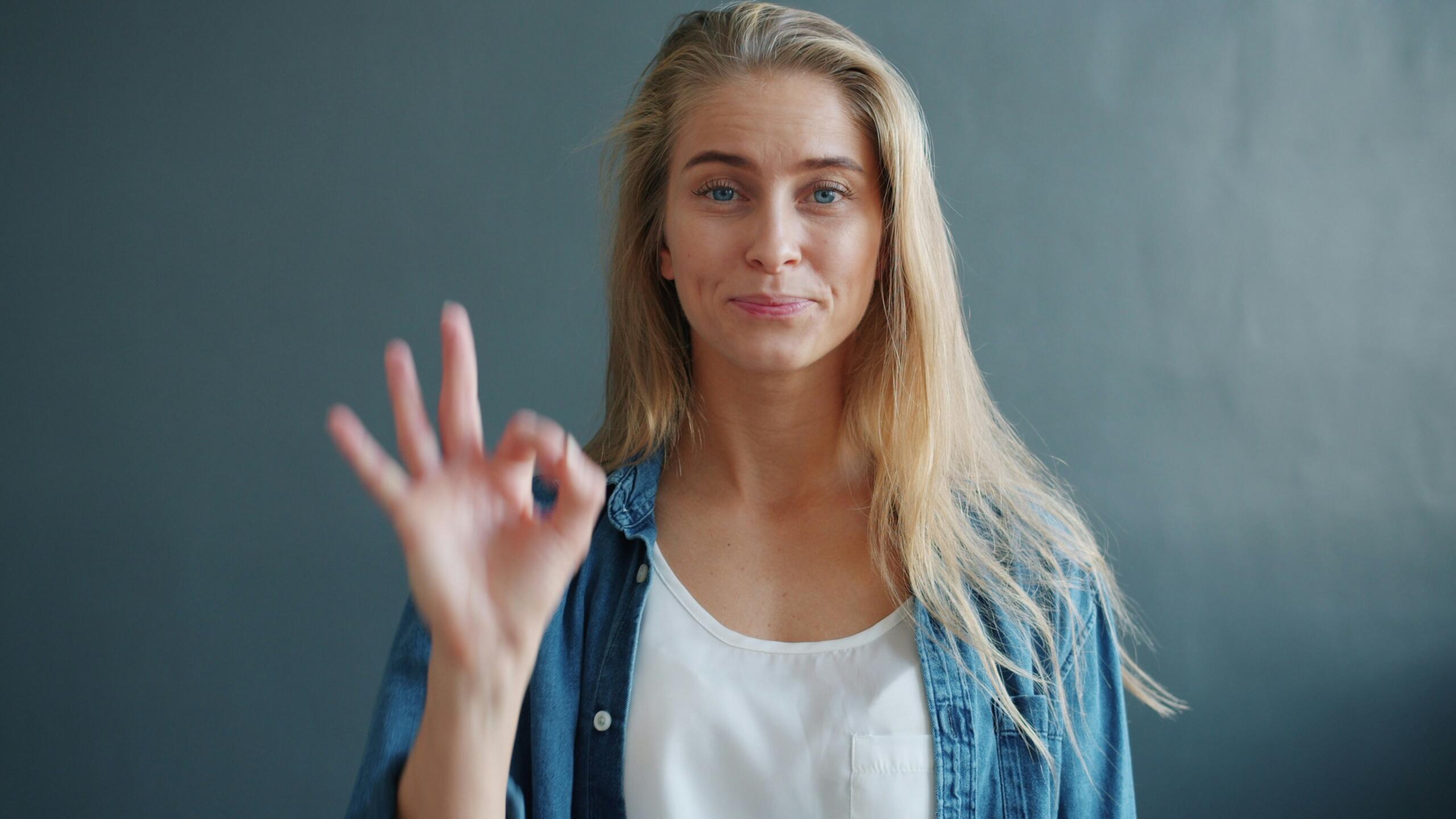 A girl with blonde hair signing okay in ASL.