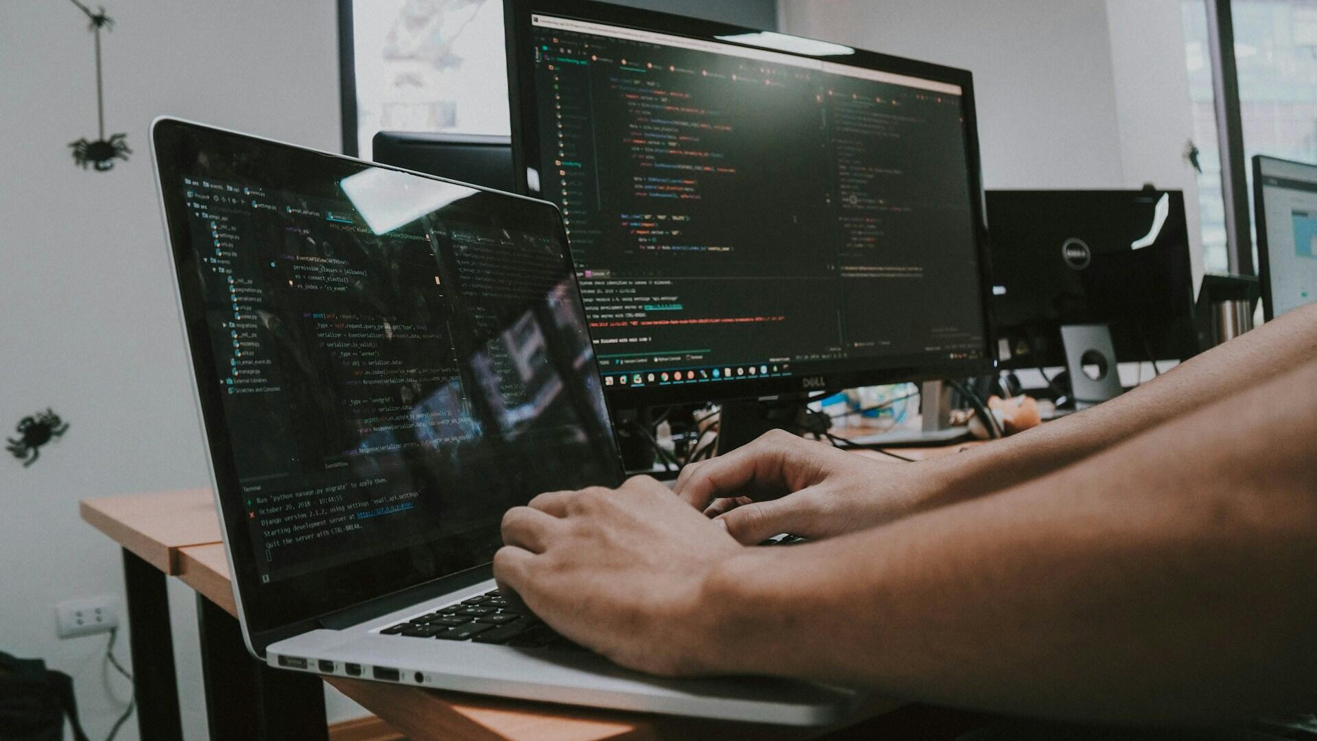 Someone typing on a computer with a monitor next to it.