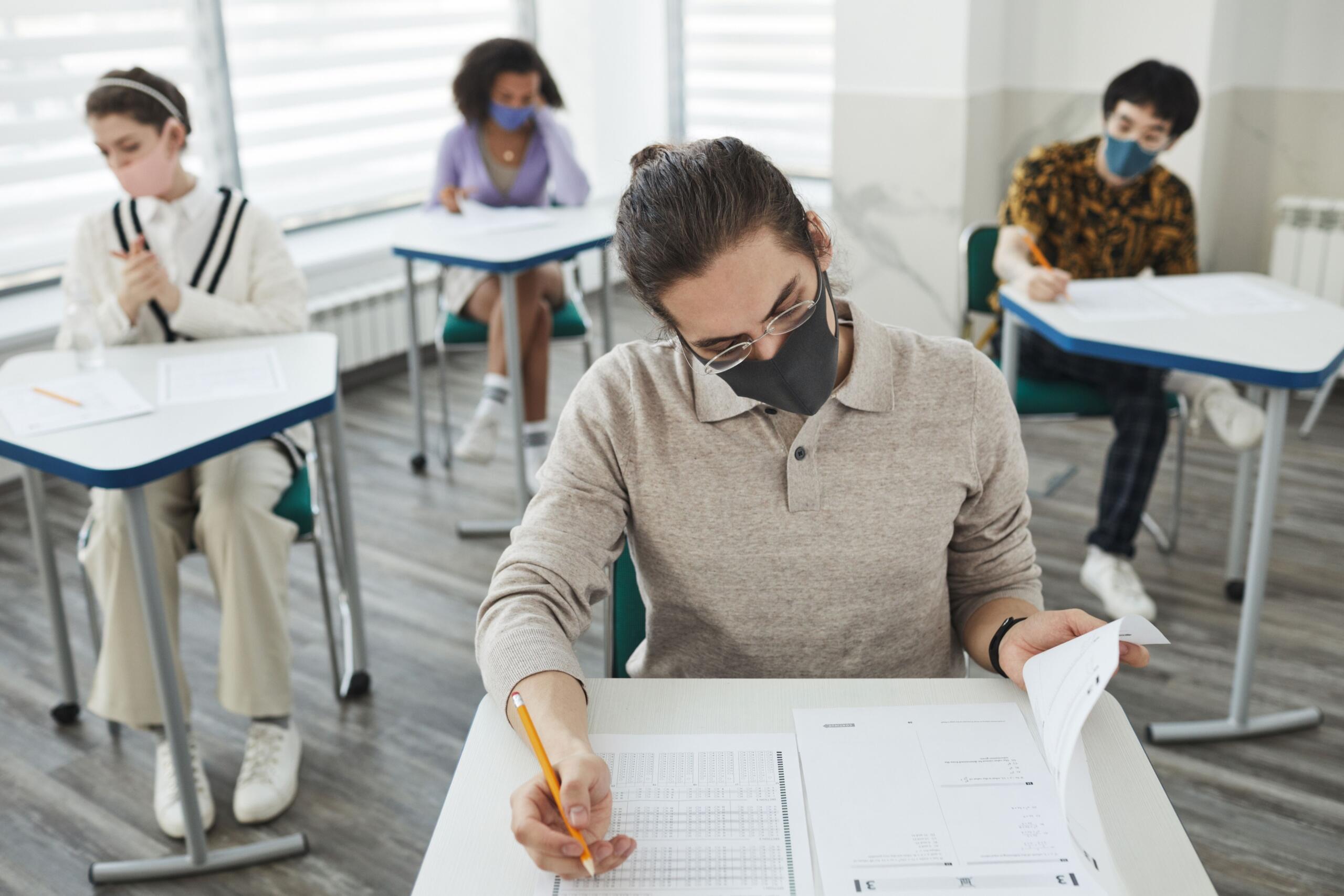 Four students wearing masks while taking exams at their desks.