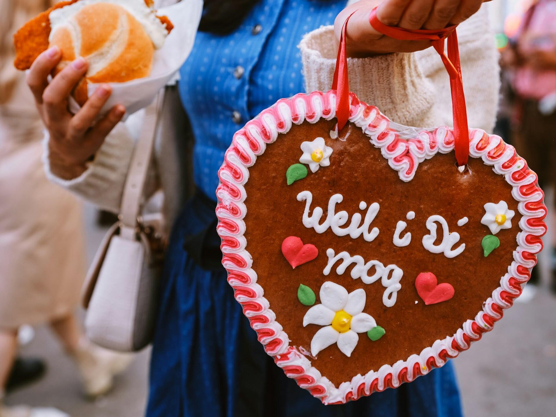 A girl in a blue dress holding up a traditional German heart-shaped cookie.
