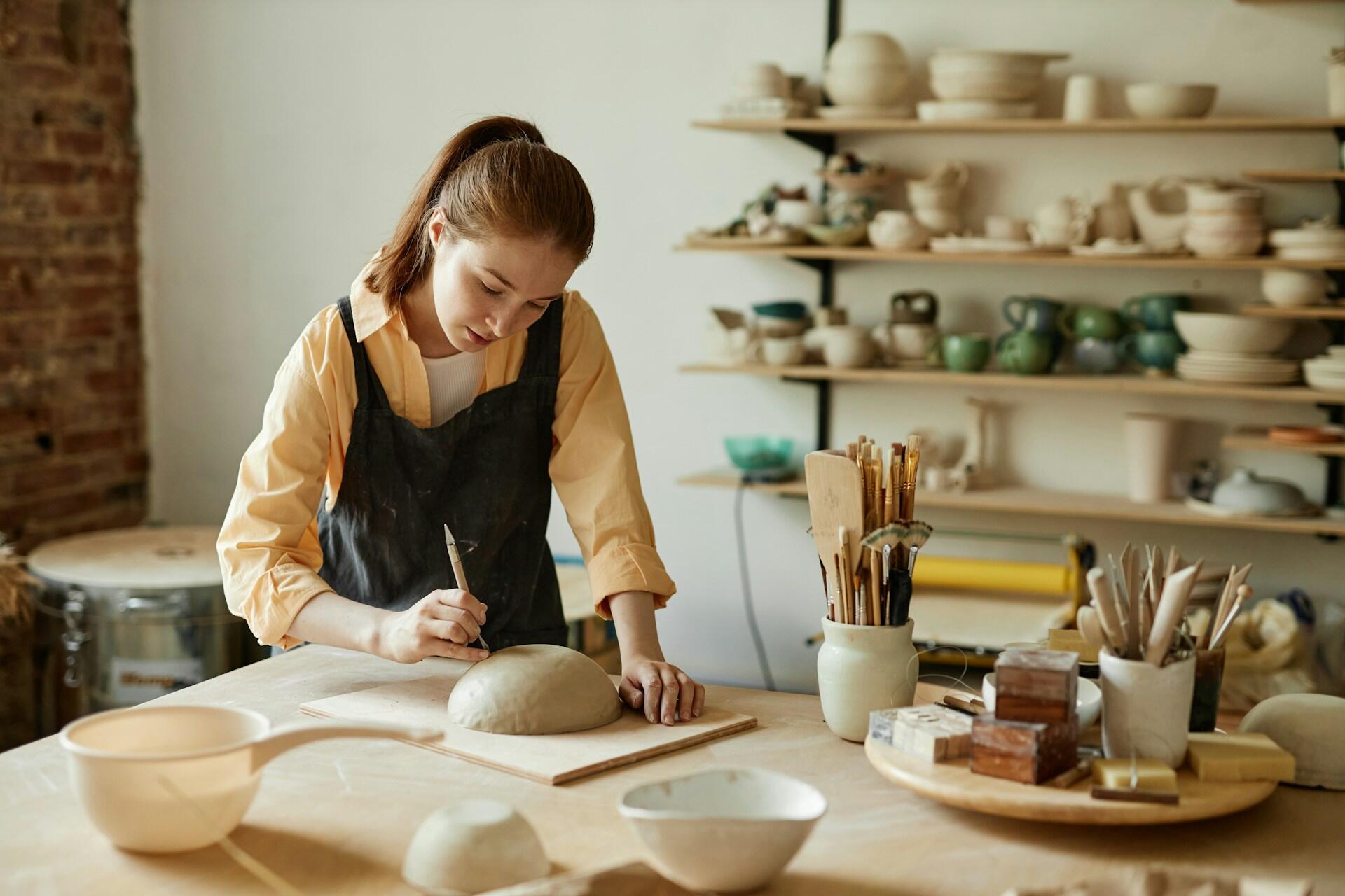 A young girl scoring the bottom of her pottery dish.