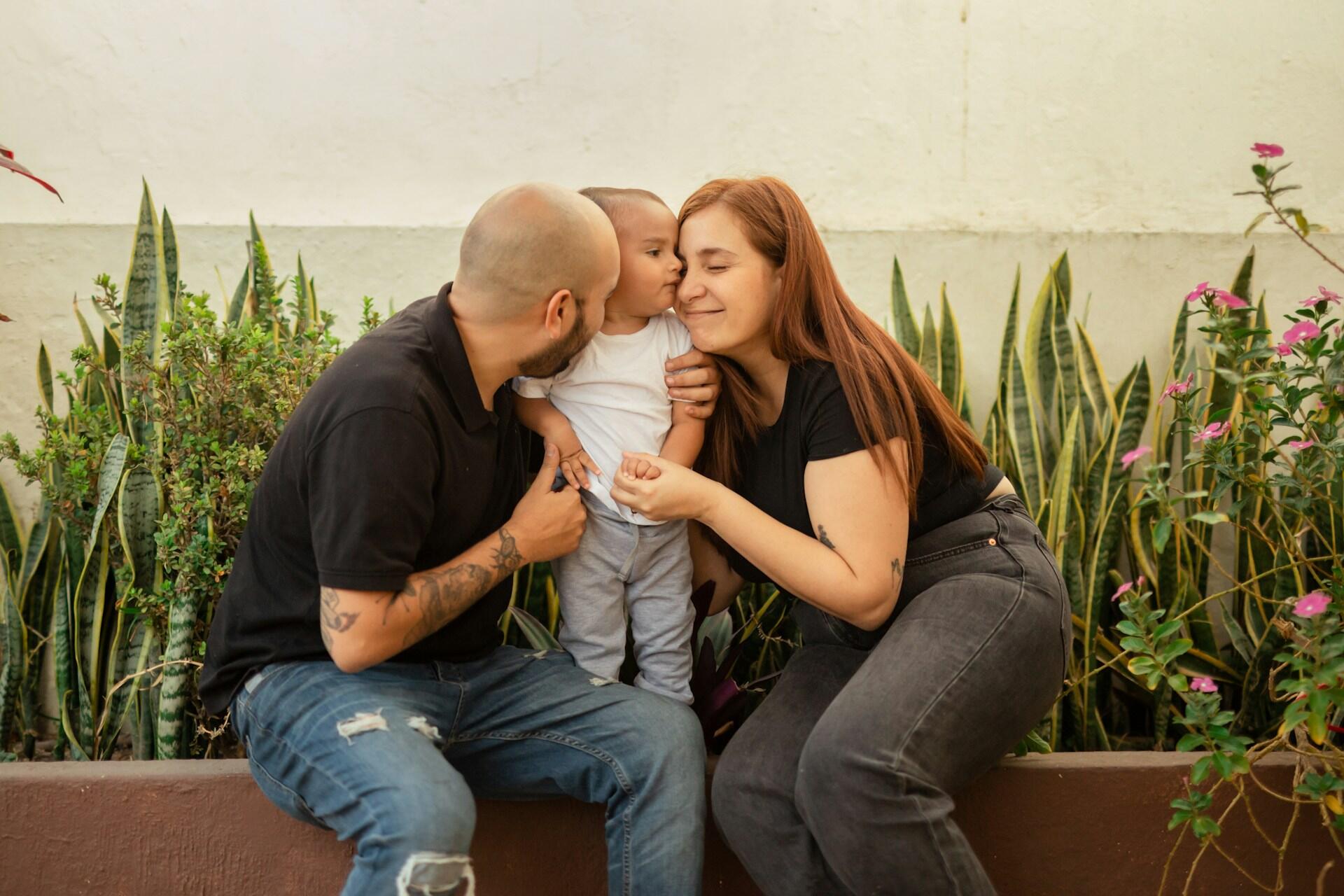 Two parents hugging their child in front of plants.