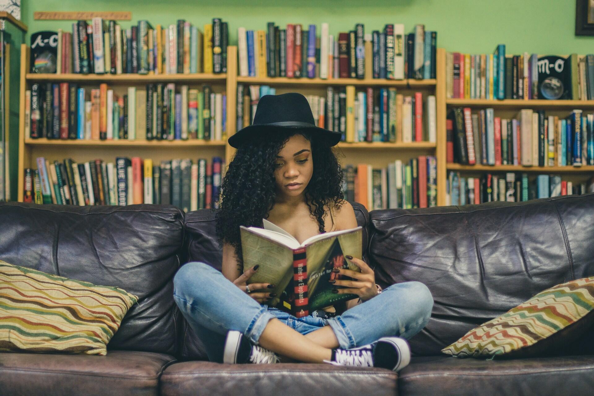 a student reading a novel on a couch in a library or bookstore