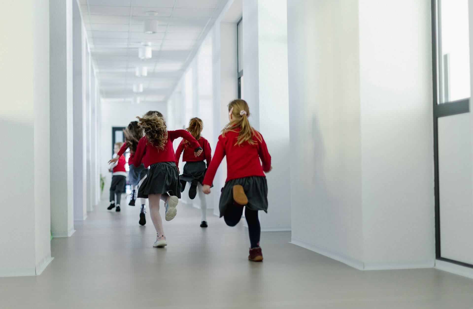 Young students in red uniforms running down the hallway.