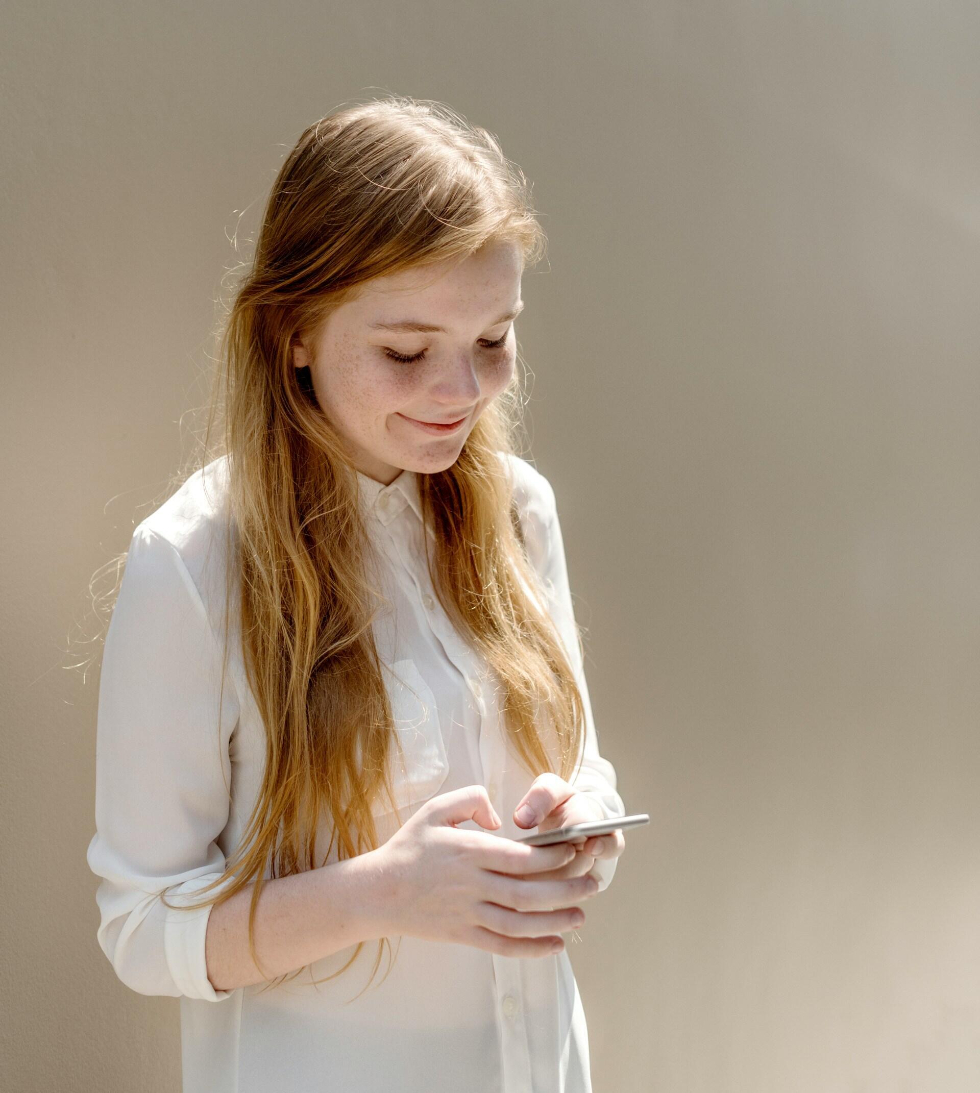 A person with red hair wearing a white shirt uses a smartphone.