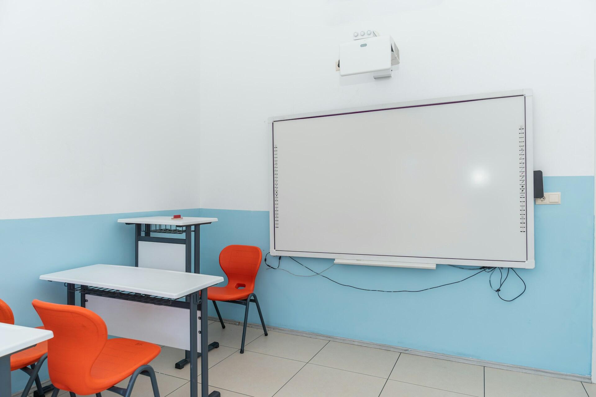 A white board in a classroom with orange chairs.