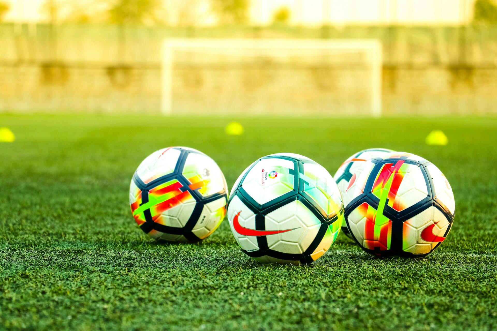 Three soccer balls on a green field in front of a goal.
