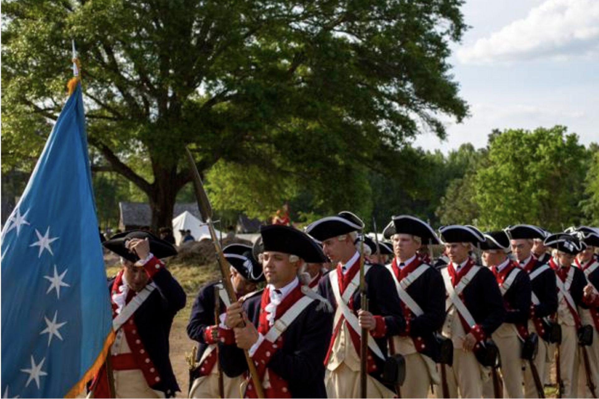 Revolutionary War reenactors in Continental Army uniforms marching with a blue flag.