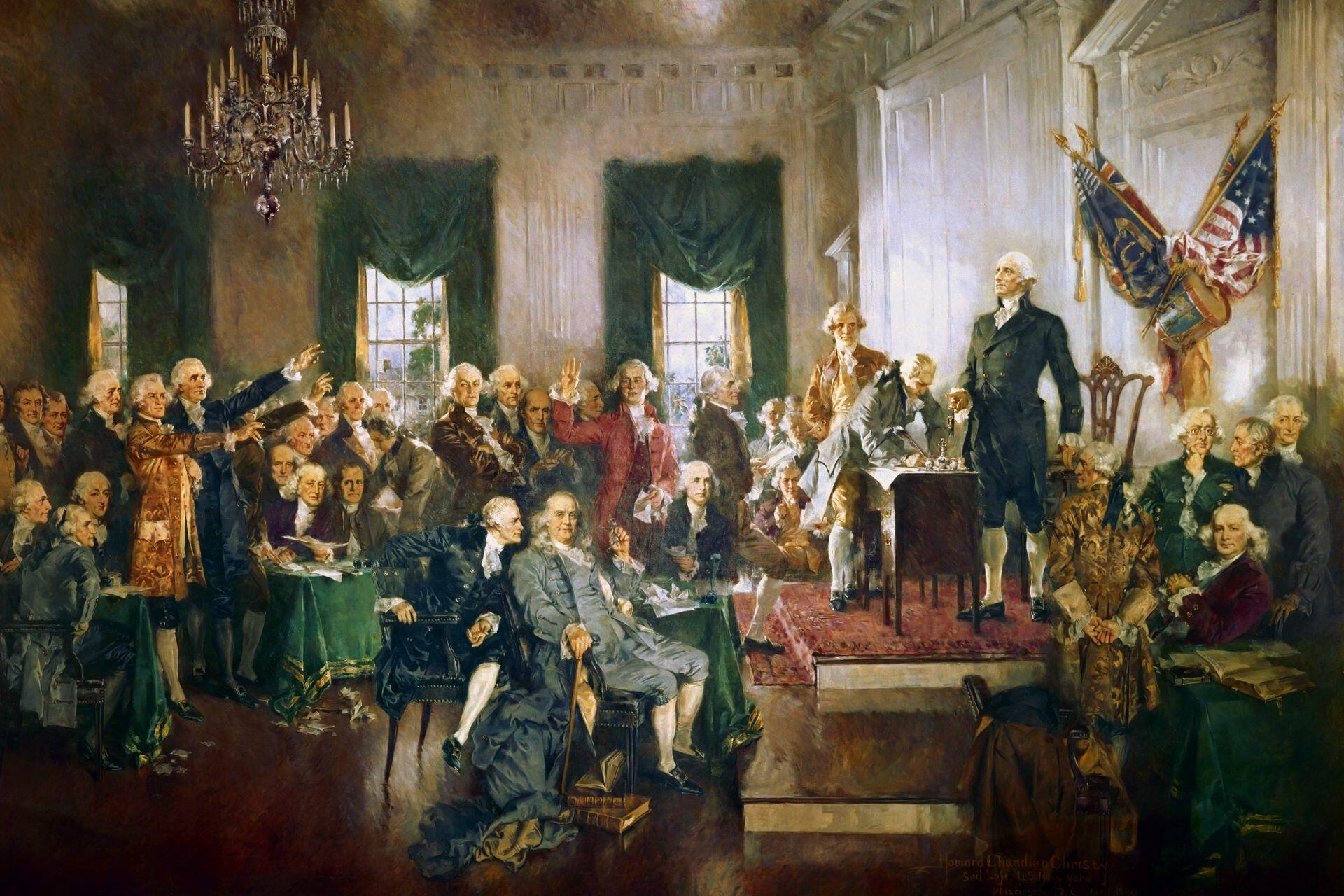 Painting of the signing of the United States Constitution with George Washington standing beside a table and delegates gathered in the room.