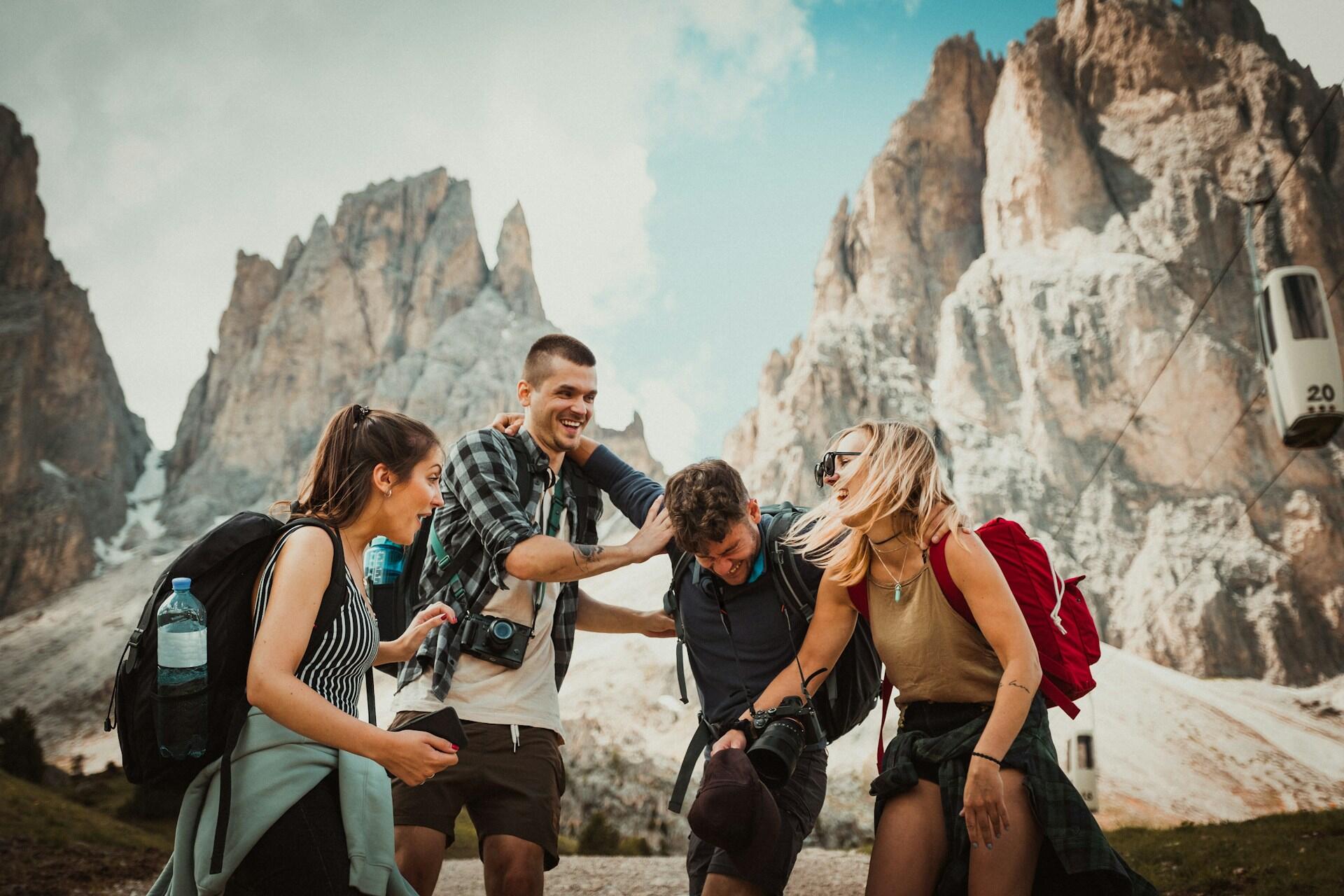 Four people with backpacks laughing in front of rocky mountains