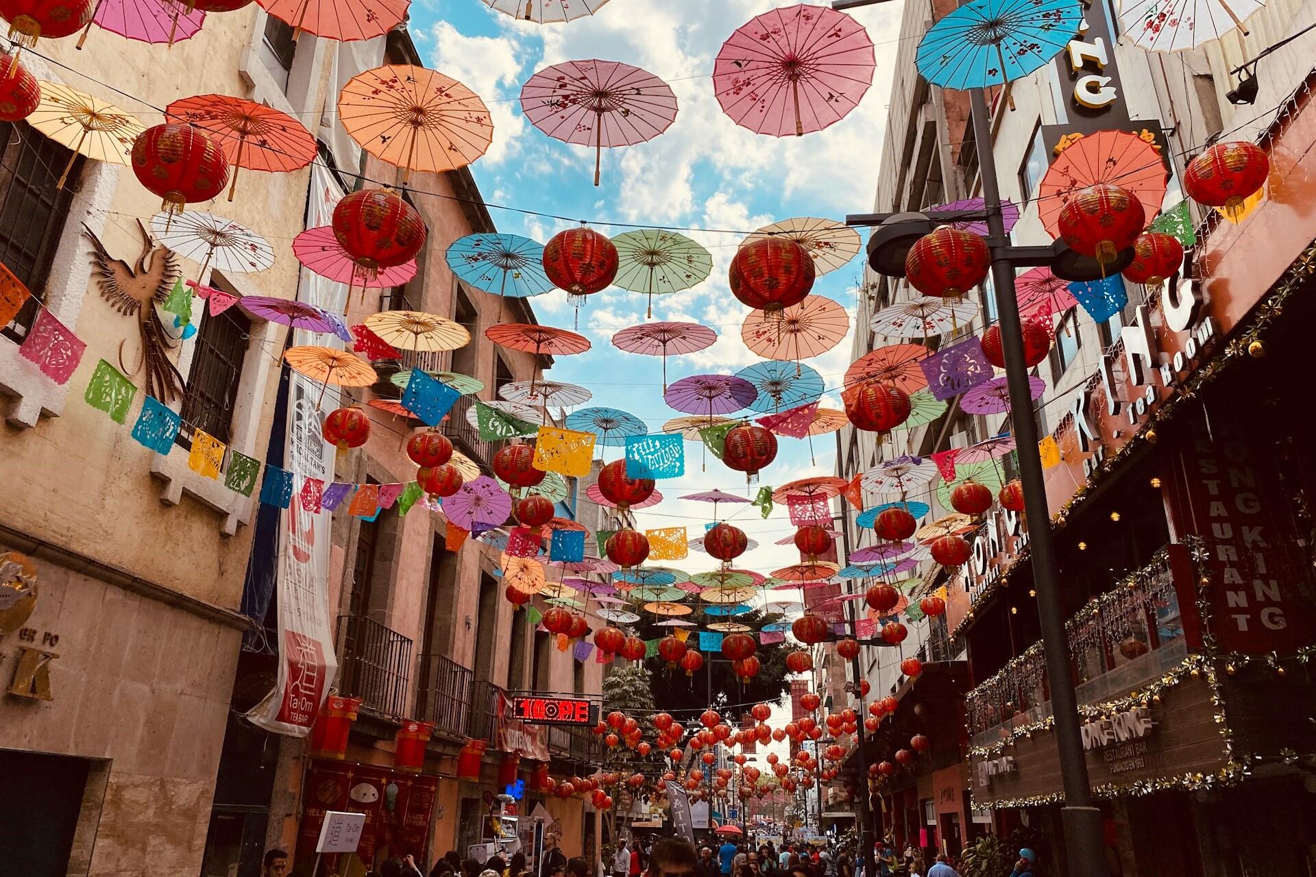 Narrow street decorated with colorful umbrellas, paper banners, and red lanterns