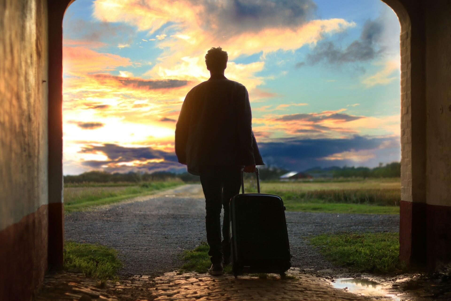 Person standing with a suitcase in an archway at sunset