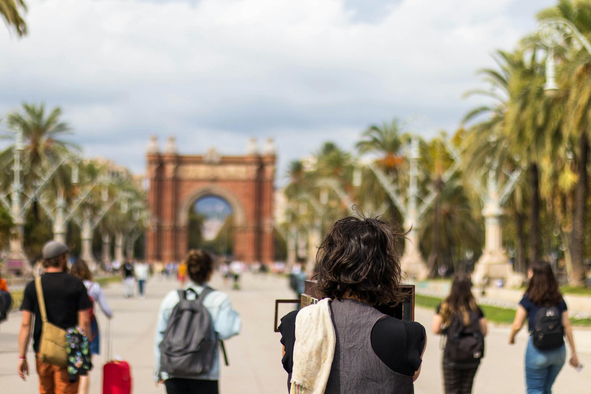 People walking along a palm-lined boulevard toward a large brick arch