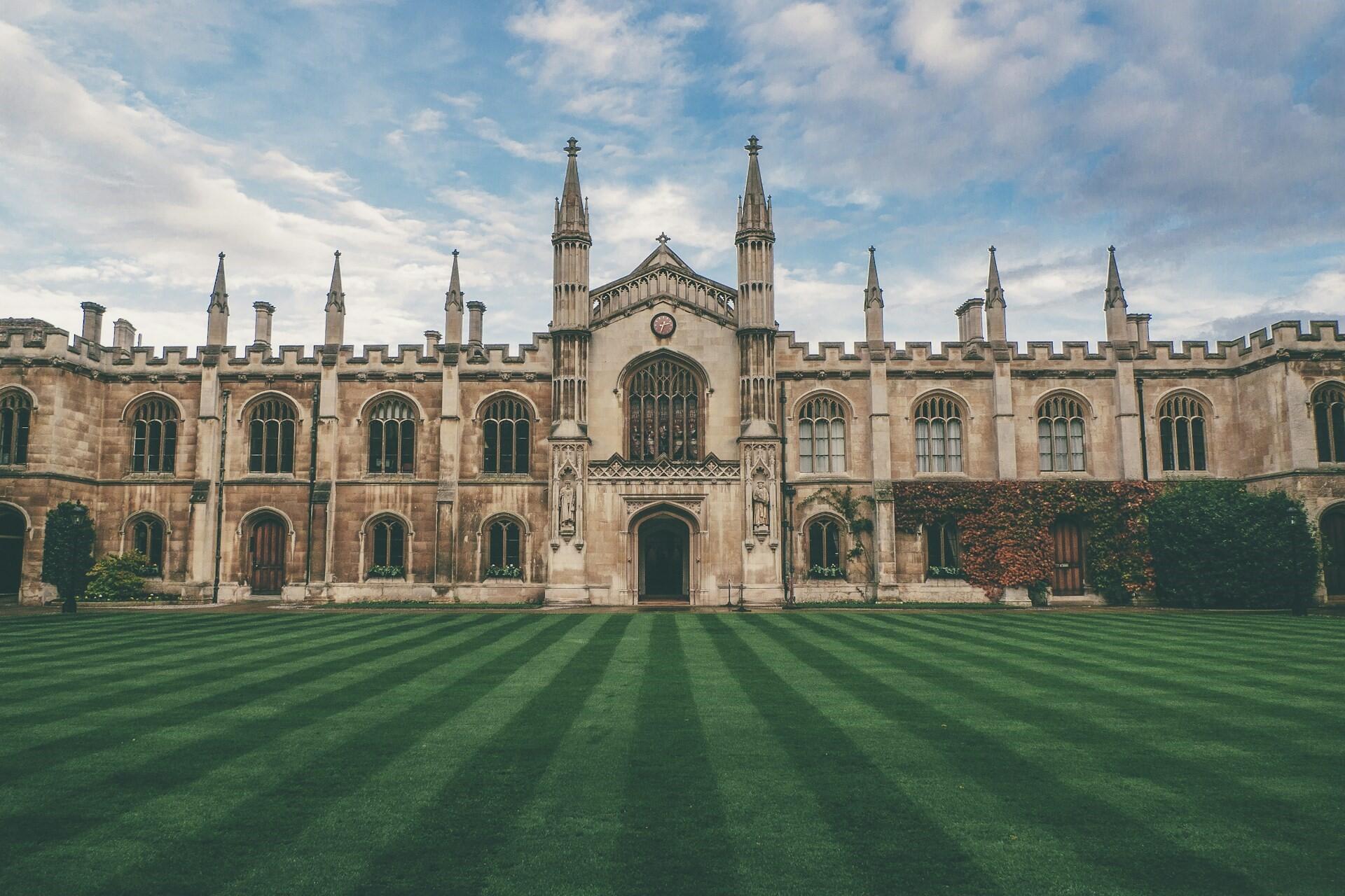 Historic university building with a striped lawn and cloudy sky