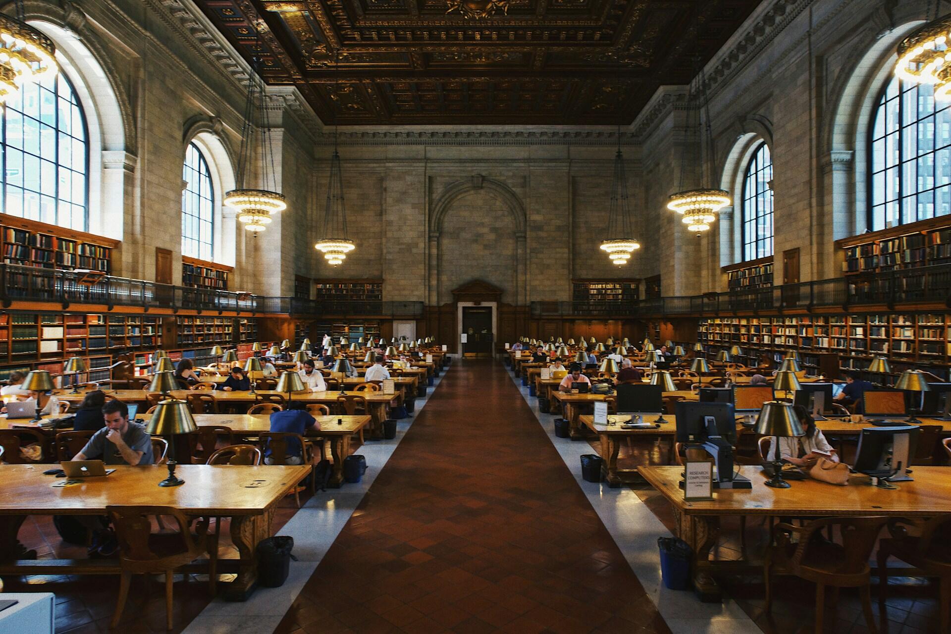 People studying at long tables in a large library reading room