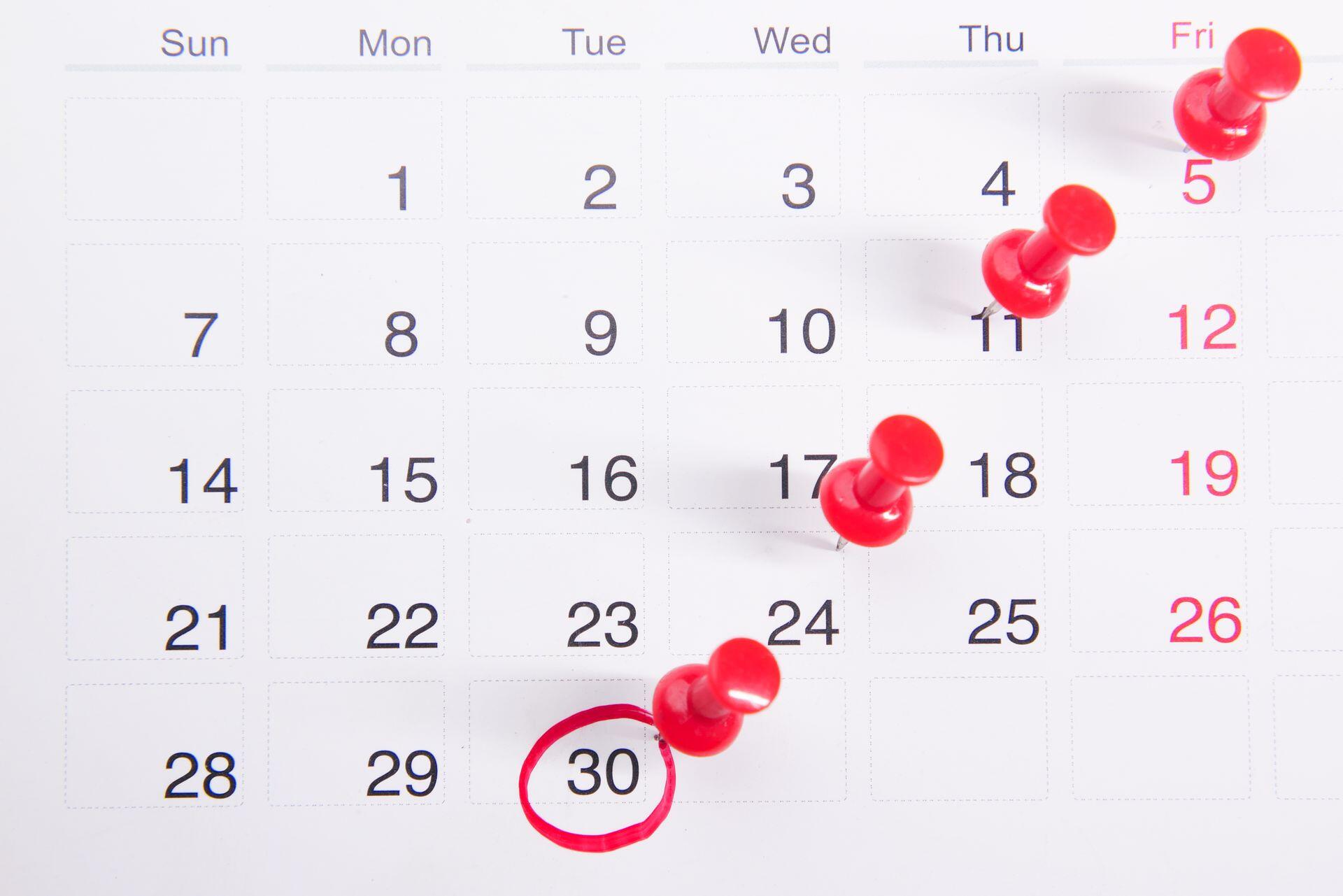 paper calendar with red push pins on certain dates, and one specific date circled in red
