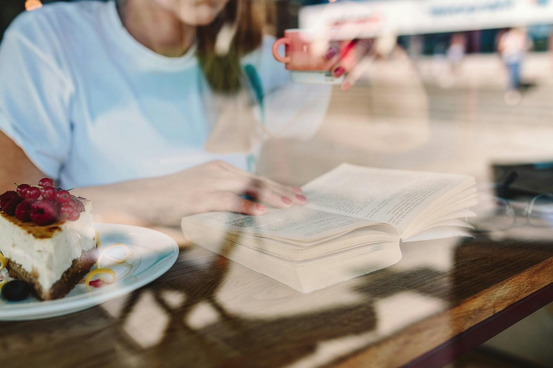 person reading a study book while drinking coffee and having a slice of cake at a cafe
